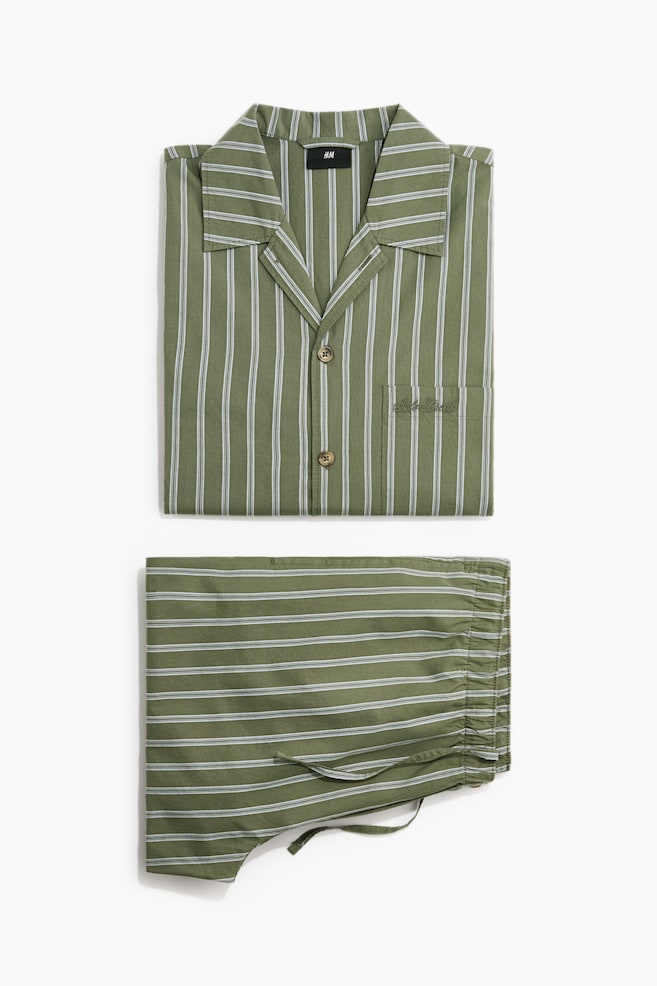 Das Pyjama-Set zeigt ein grünes Oberteil und passende Unterteile, beide mit weißen Streifen. Die Vorderseite des Oberteils zeigt einen Umlegekragen, eine französische Knopfleiste mit zwei braunen Knöpfen und eine Brusttasche mit 'Sleep Break' bestickt. Die Vorderseite der Unterteile verfügt über einen elastischen Bund mit sichtbarem Kordelzug und einen dekorativen braunen Knopf. - 1