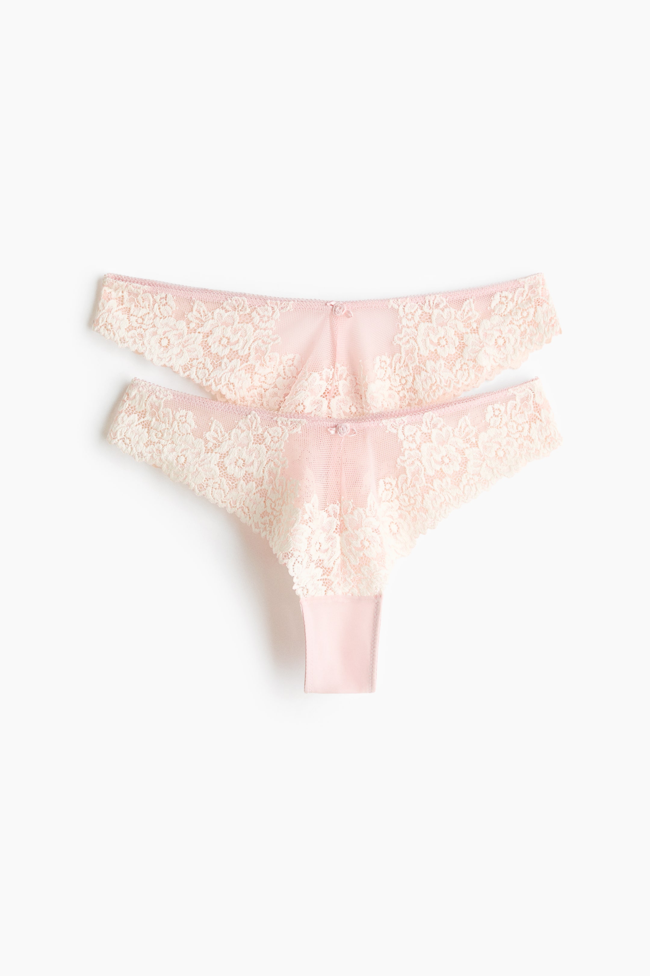 Vis større bilde: To truser presenteres forfra, som overlapper hverandre litt. De er laget av off-white blonder over lys rosa mesh, med en lav, V-formet midje med en liten sløyfe i midten, en foret kile og en høy skjæring bak.