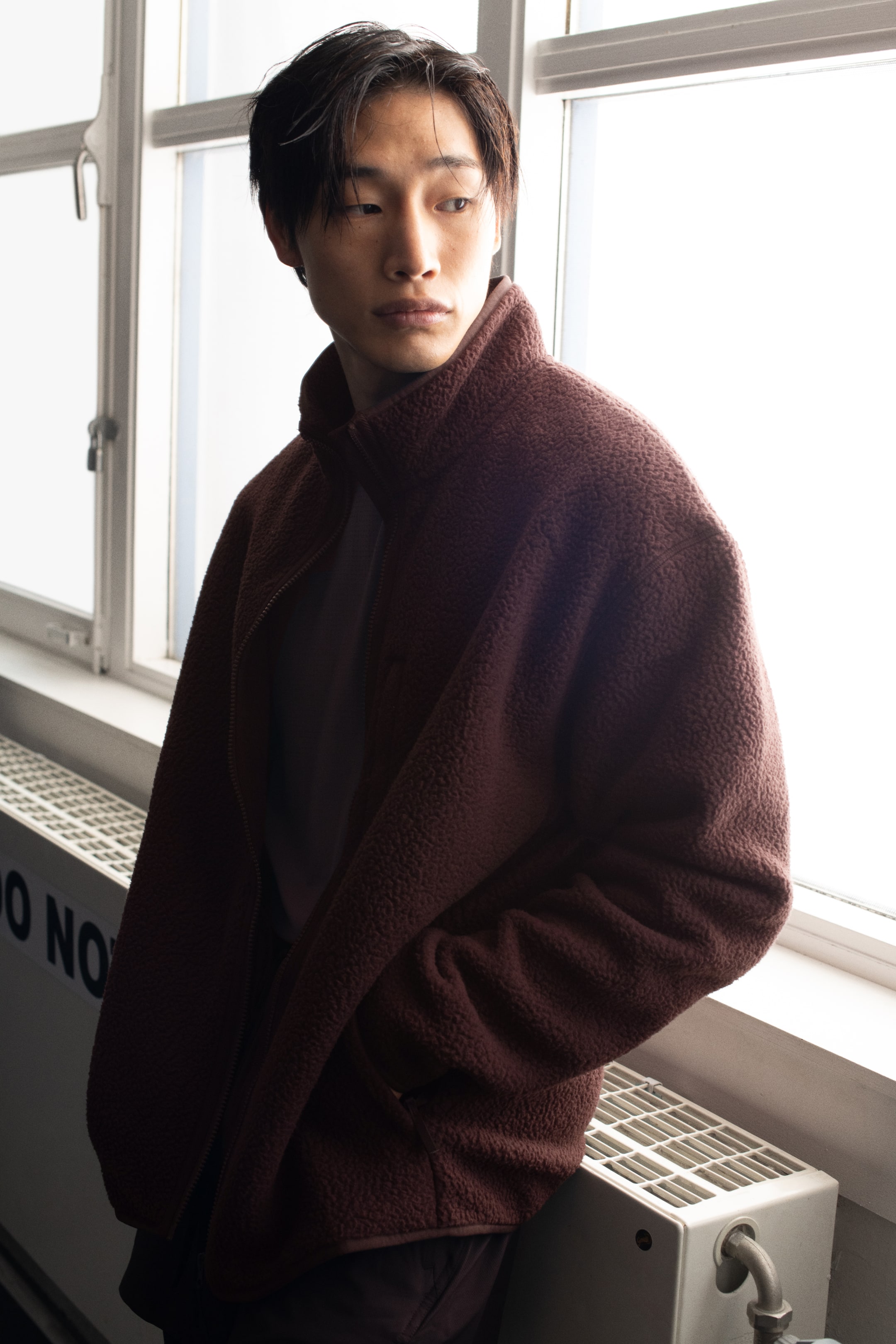 View larger image: A dark reddish-brown fleece jacket is featuring a high stand-up collar and a full-zip front closure, seen from a slightly angled front view. The jacket is made from a soft, fuzzy material and includes visible side pockets, with a lighter t-shirt underneath.