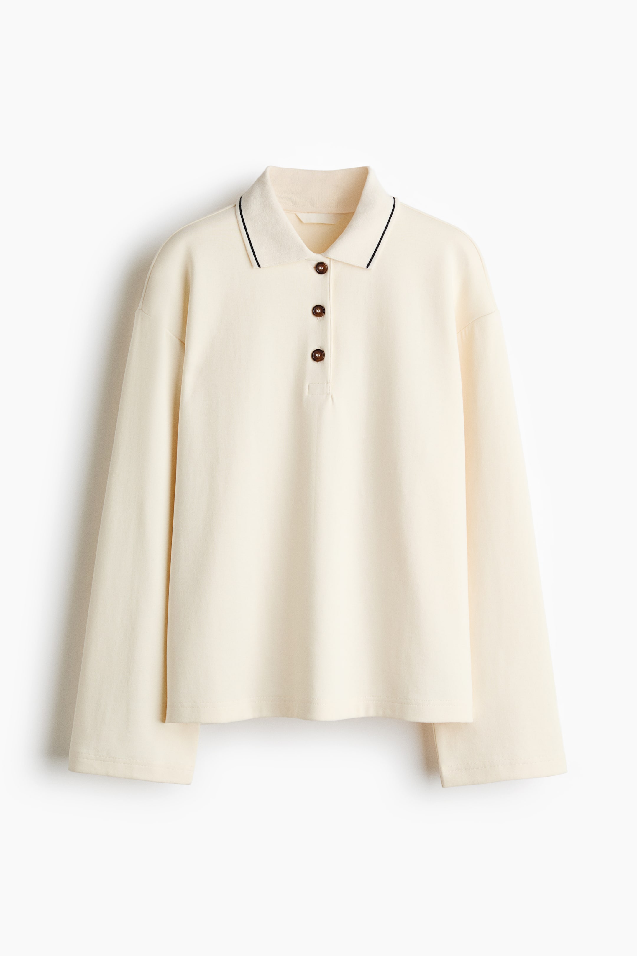 View larger image: A cream long-sleeved polo shirt features a pointed collar accented with a thin black stripe, a three-button placket with dark brown buttons, and a relaxed fit with long sleeves and a straight hem.
