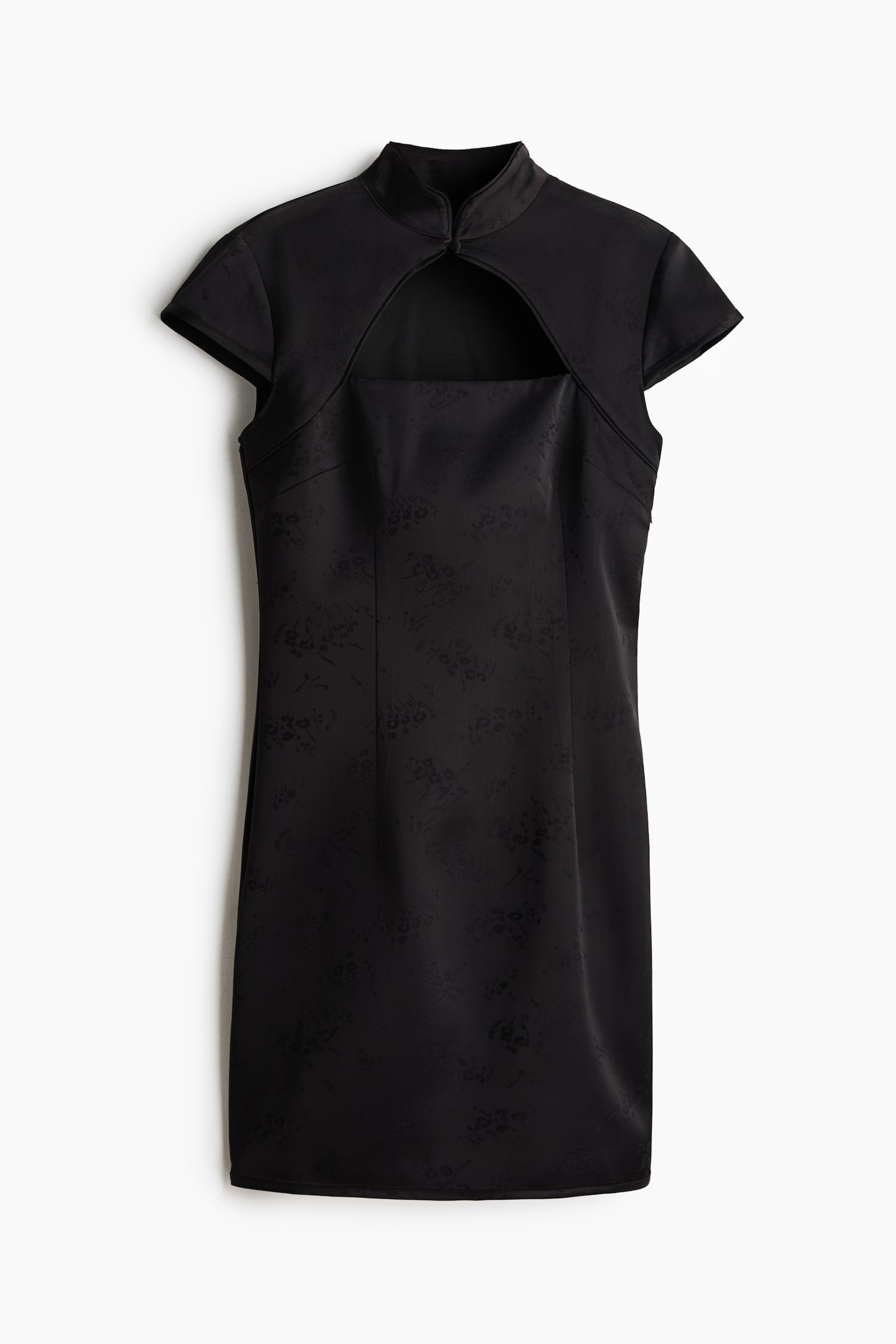 A short, fitted black dress in a jacquard weave is facing front, showcasing a band collar with a front fastening, a large cut-out section on the chest, and cap sleeves. The garment is displaying a subtle floral pattern with vertical shaping darts defining the waist.