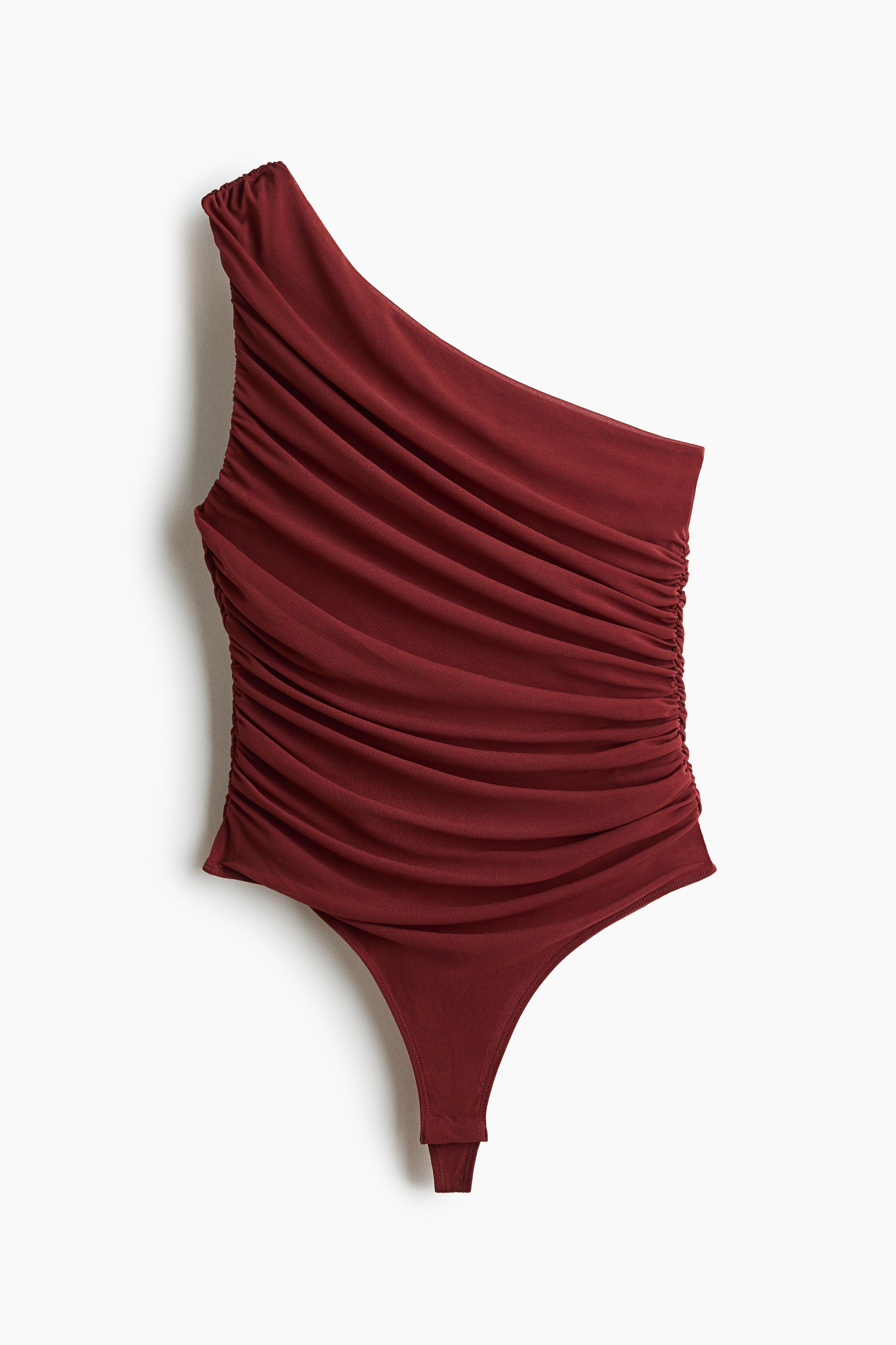 A dark red one-shoulder bodysuit featuring gathered, draped detailing across the front and an asymmetric neckline is being worn by the model. The bodysuit is paired with low-waisted black trousers, with the model holding a thin silver chain belt at the waistband.