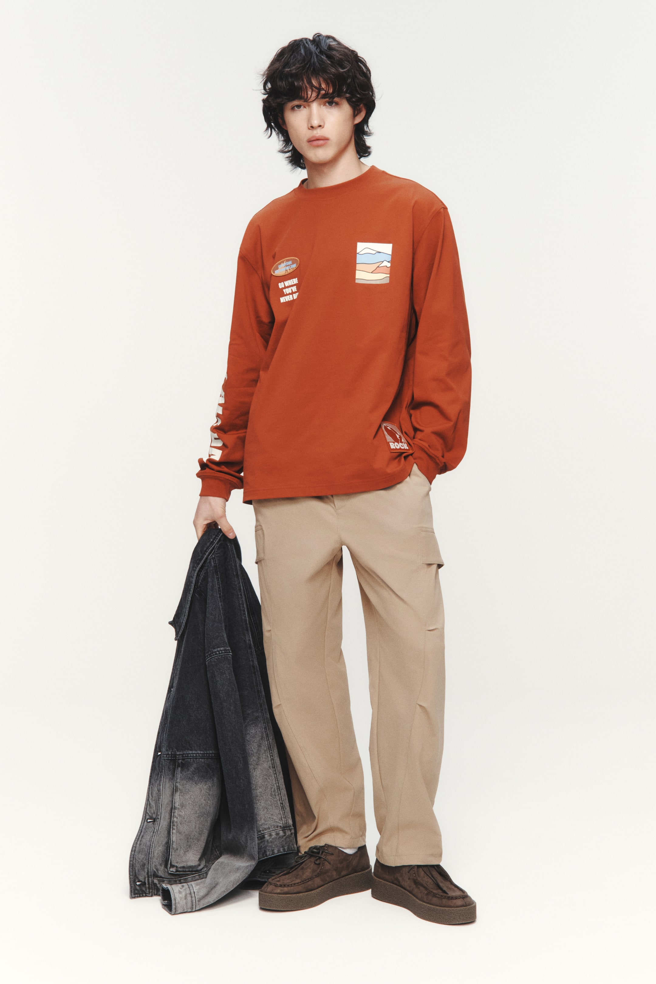 Xem ảnh lớn hơn: Người mẫu đang mặc quần cargo màu be làm từ vải twill mềm mại, với các túi chéo bên hông, nếp gấp ở đầu gối và túi nắp ở ống quần. Quần có kiểu dáng rộng rãi, và tay phải của người mẫu đang đặt trong túi chéo bên hông.