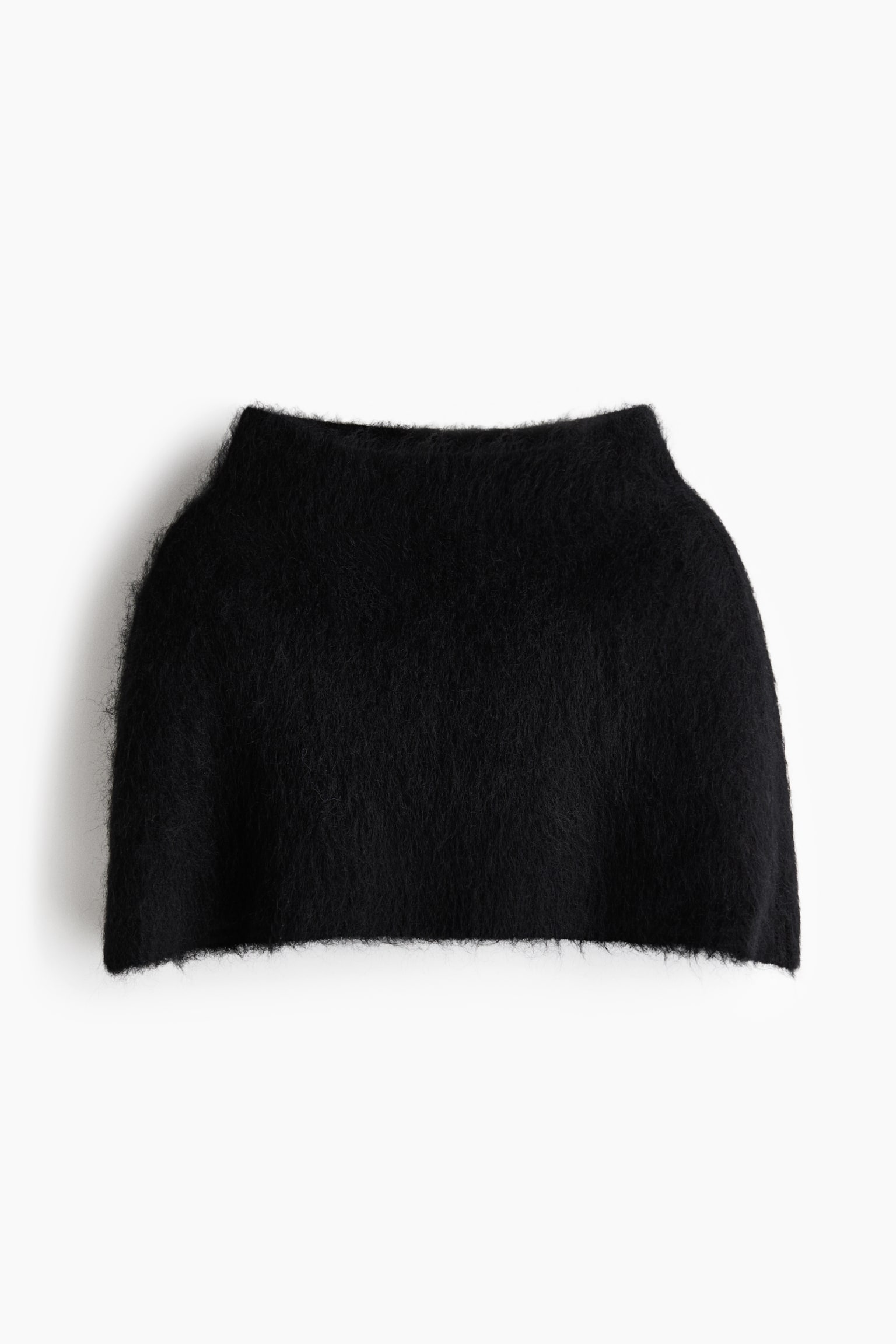 Una minifalda de punto negra y peluda estÃ¡ orientada hacia el frente, mostrando una tela muy texturizada y desgreÃ±ada con un acabado tipo mohair. La prenda presenta una abertura superior mÃ¡s estrecha y un dobladillo inferior recto ligeramente mÃ¡s ancho.