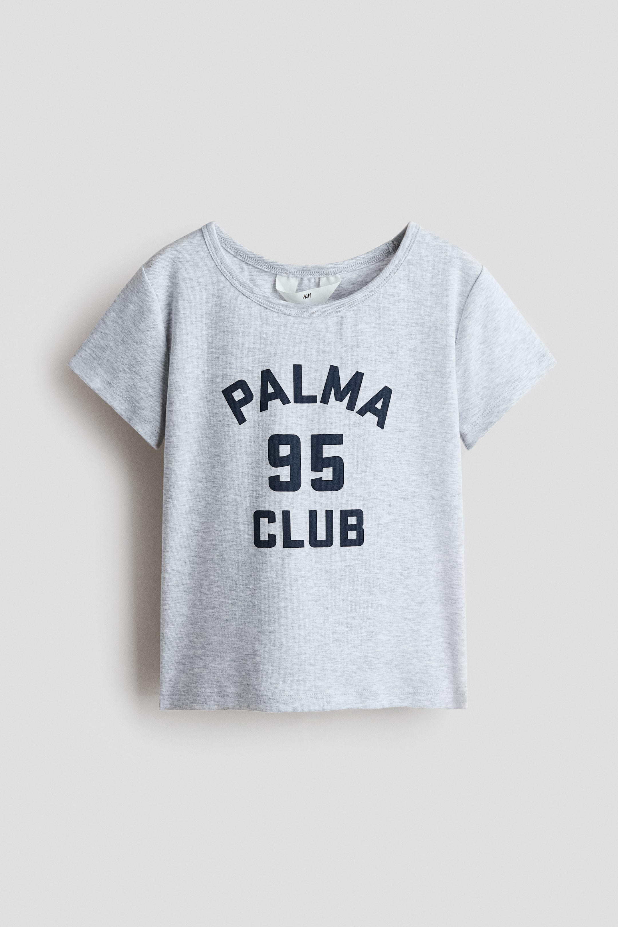 Se større billede: En frontvendt T-shirt i lys grå blød jersey med et mørkeblåt "PALMA 95 CLUB" print på brystet og en ribbet kant rundt halsudskæringen.