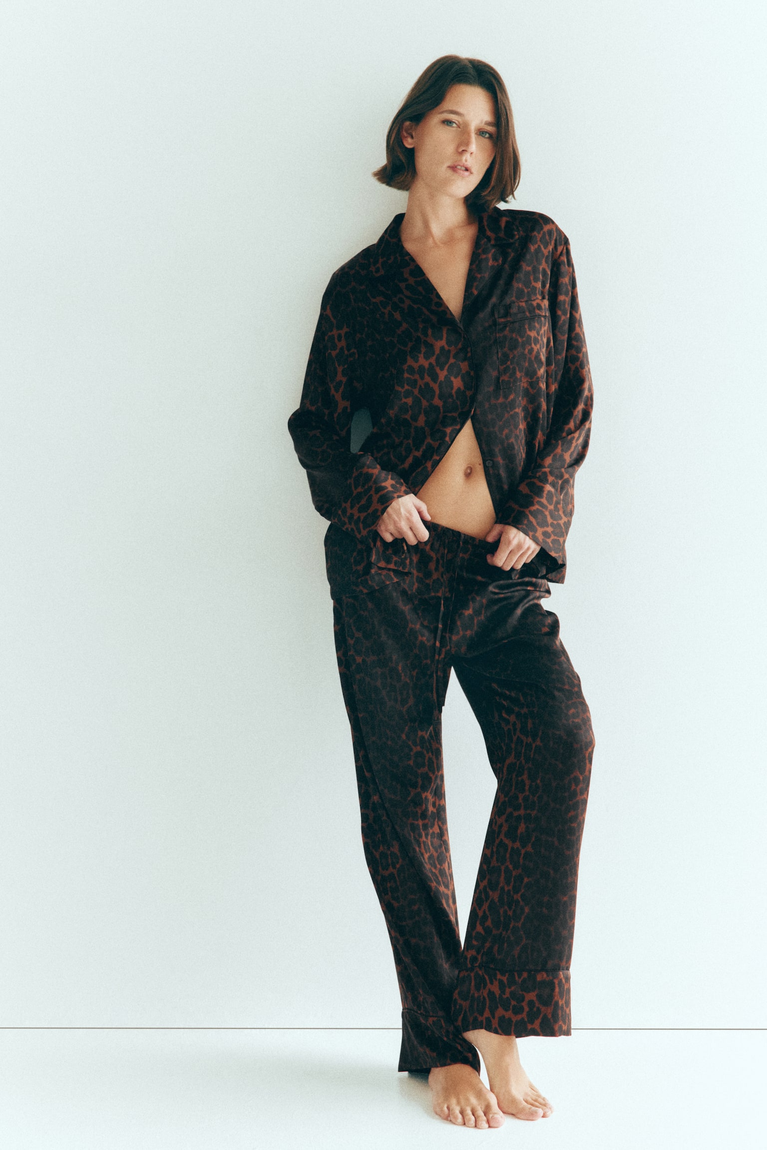 Model, uzun kollu bir gÃ¶mlek ve uyumlu geniÅ paÃ§a pantolondan oluÅan leopar desenli saten bir pijama takÄ±mÄ± giyiyor. GÃ¶mleÄin alt kÄ±smÄ± kÄ±smen dÃ¼Ämesiz bÄ±rakÄ±lmÄ±Å ve model pantolonun bel kÄ±smÄ±nÄ± tutuyor. - 1