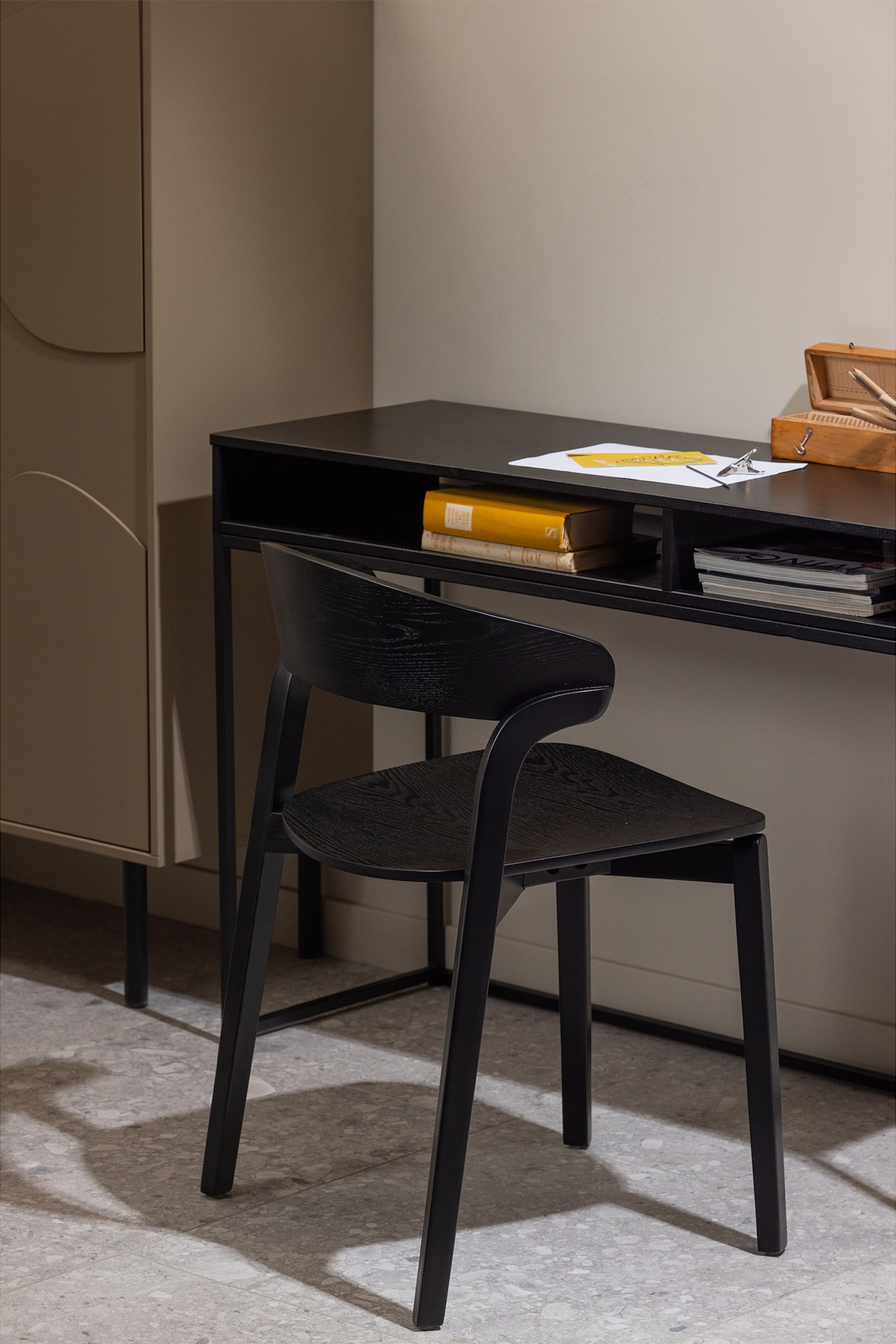 Een zwarte houten stoel staat in een lichte hoek, waarbij de gebogen rugleuning en de gevormde zitting met zichtbare houtnerf worden getoond. De stoel heeft vier rechte poten en staat onder een zwart bureau. - 1