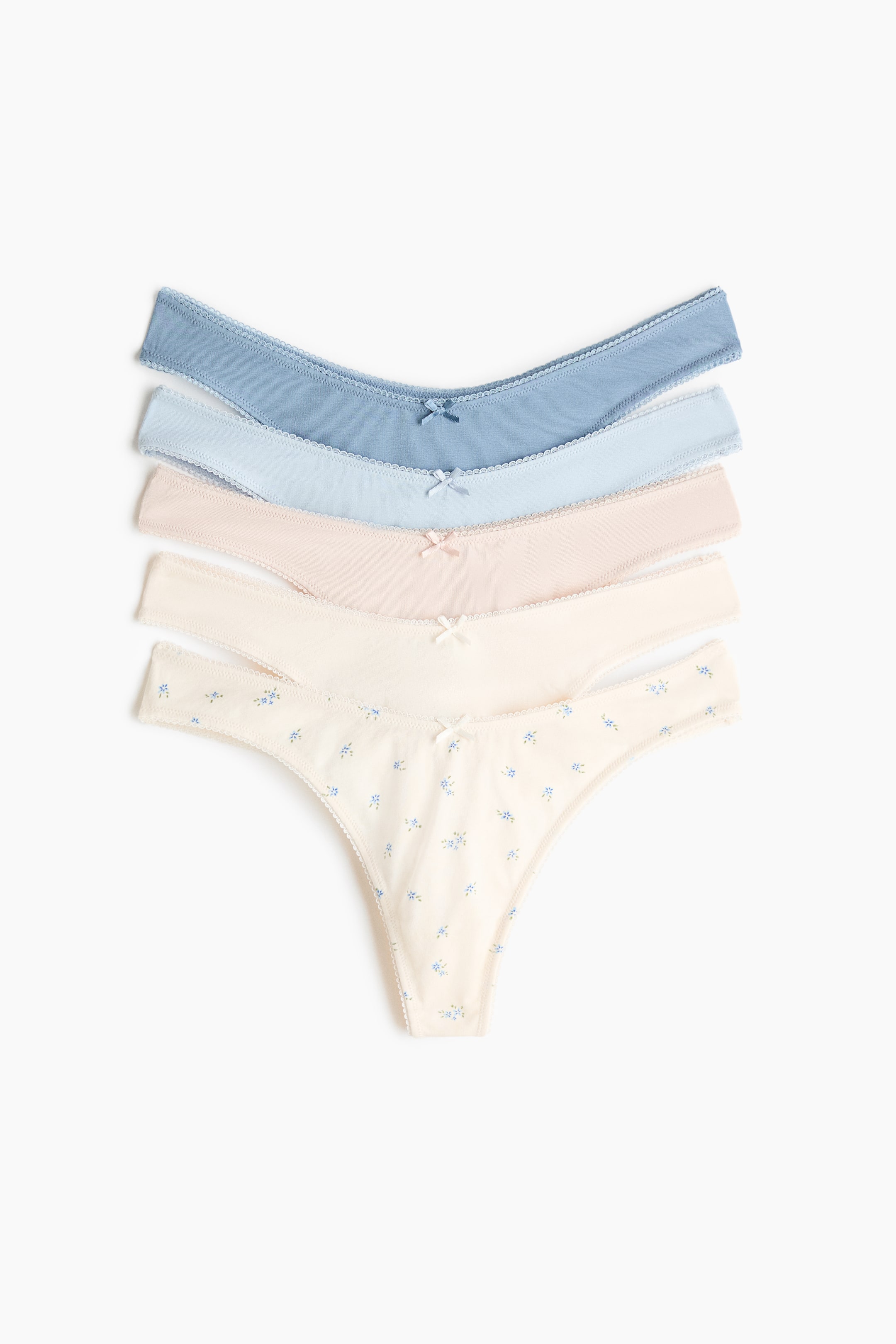 View larger image: Five cotton jersey thong briefs are fanned out and stacked, displaying their front views. Each brief features a low, V-shaped waistline, a small bow at the centre front, and scalloped trim along the edges. They appear in varying shades of blue, nude, and cream, with one cream brief showcasing a delicate blue floral pattern.