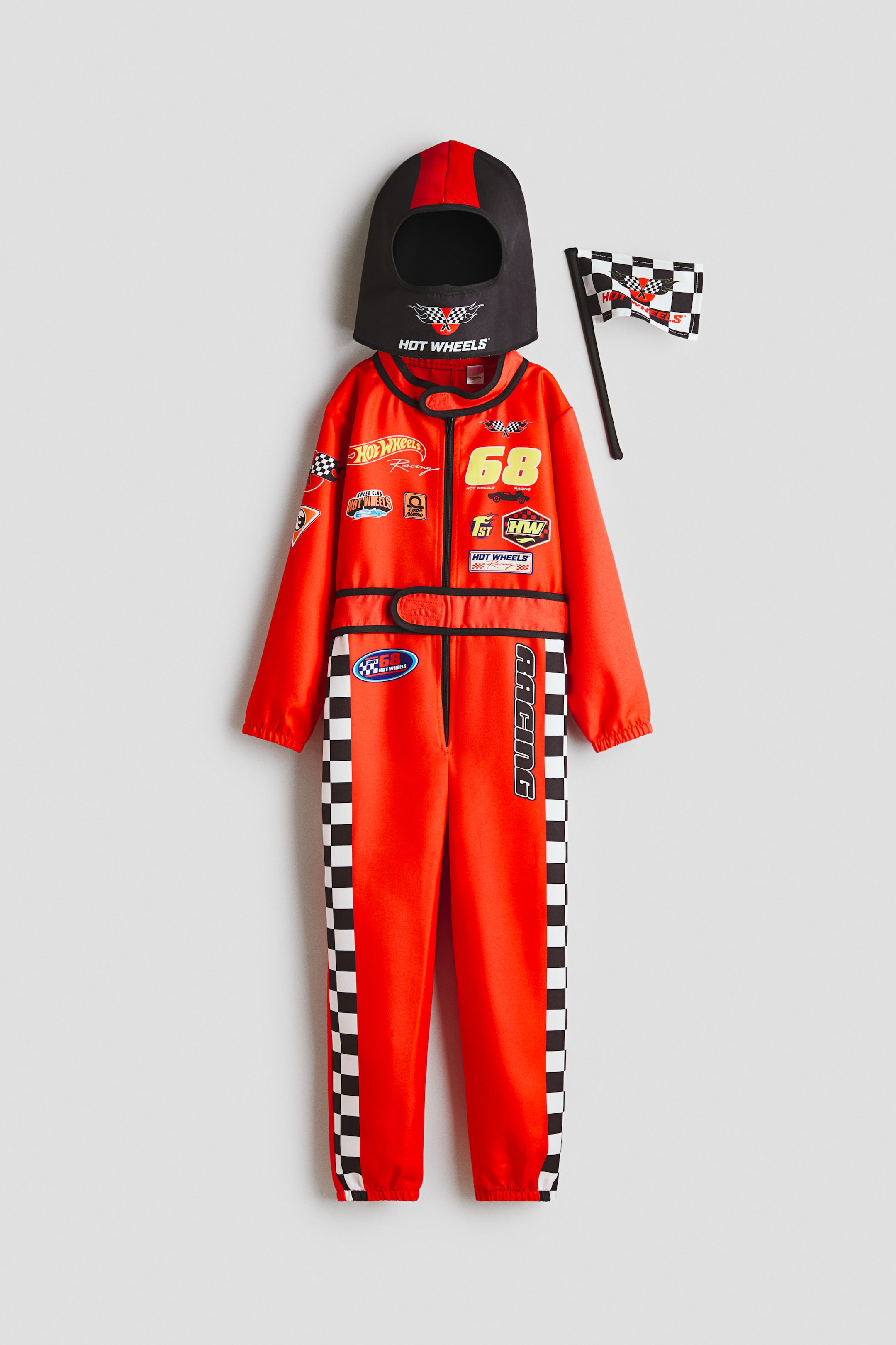 View larger image: A Hot Wheels racing costume set is presented, featuring a red jumpsuit with multiple racing patches, a yellow number ‘68’, and black-and-white chequered flag stripes along the outer legs. The set also includes a black and red helmet hood with a Hot Wheels logo and a small chequered flag.