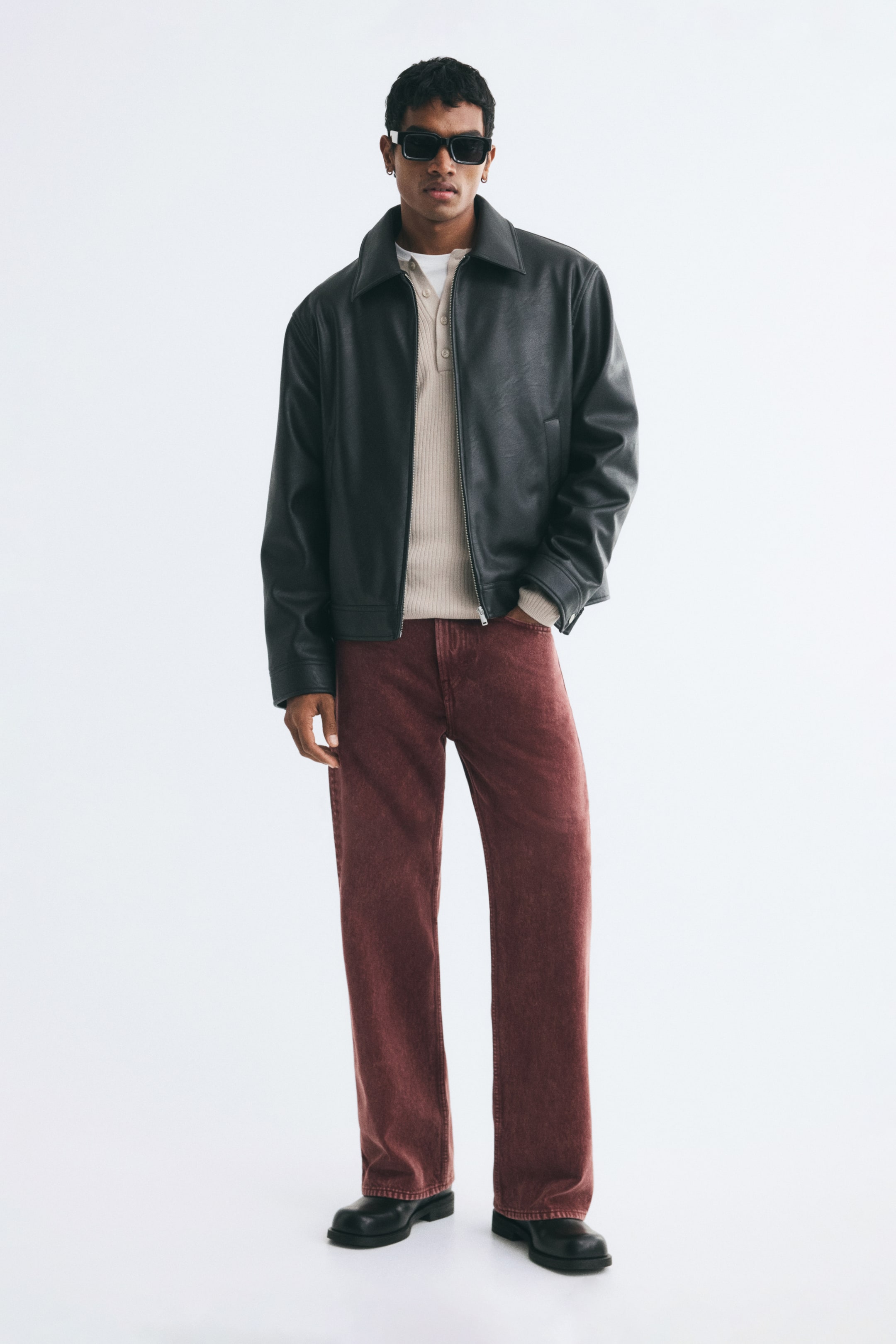 View larger image: The model is wearing reddish-brown denim jeans with a relaxed, straight-leg fit, standing with one hand tucked into a front pocket. The jeans are styled with a beige knit shirt, a black leather jacket, and black leather boots.