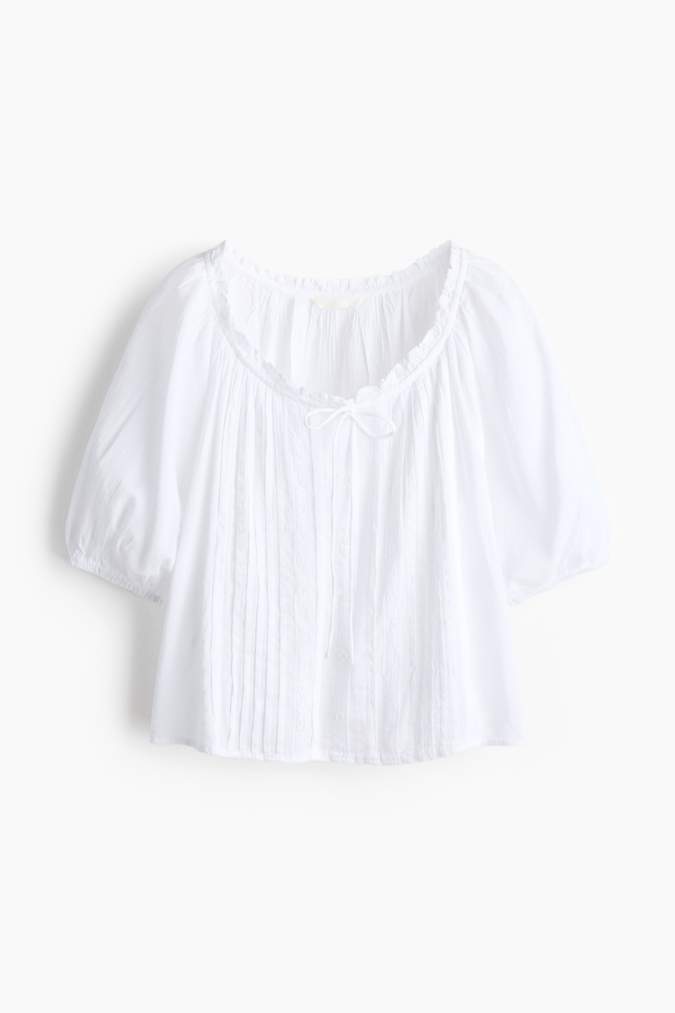 Xem ảnh lớn hơn: Một chiếc áo blouse trắng đang được trình bày phía trước, nổi bật với cổ áo rộng, xếp bèo và tay áo ngắn phồng có cổ tay co giãn. Phần trung tâm phía trước được chi tiết với các đường gân dọc, một nút thắt nhỏ và các nút cài.