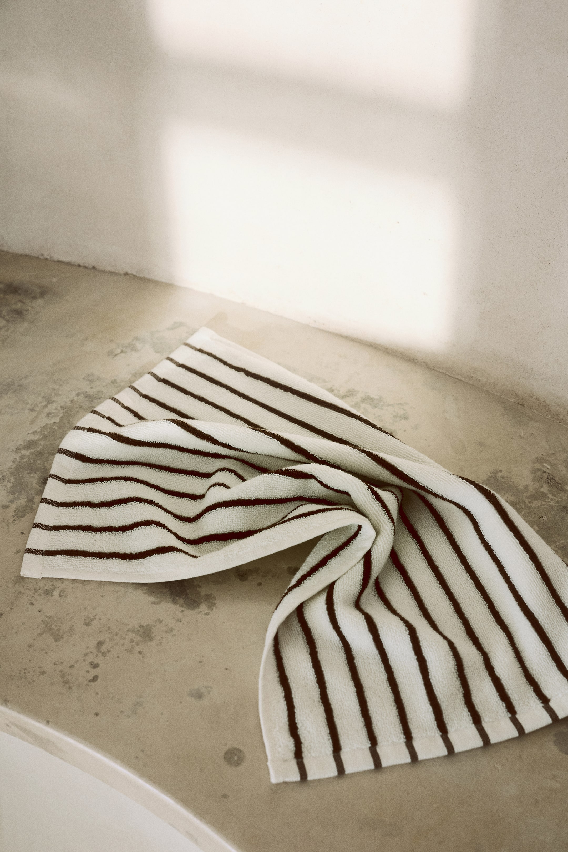 View larger image: An off-white terrycloth towel is laid draped and folded diagonally across the surface, showcasing horizontal dark brown stripes.