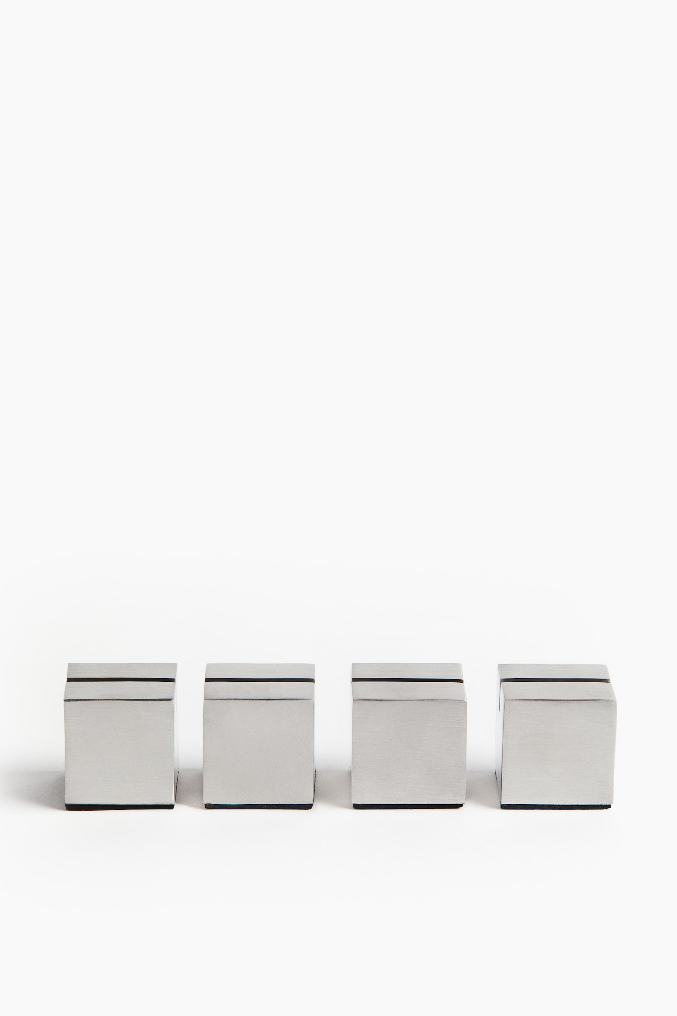 View larger image: Four place card holders are arranged front-facing, each showcasing a brushed stainless steel finish. Each sleek, rectangular block features a horizontal slot on its top surface and a dark base.