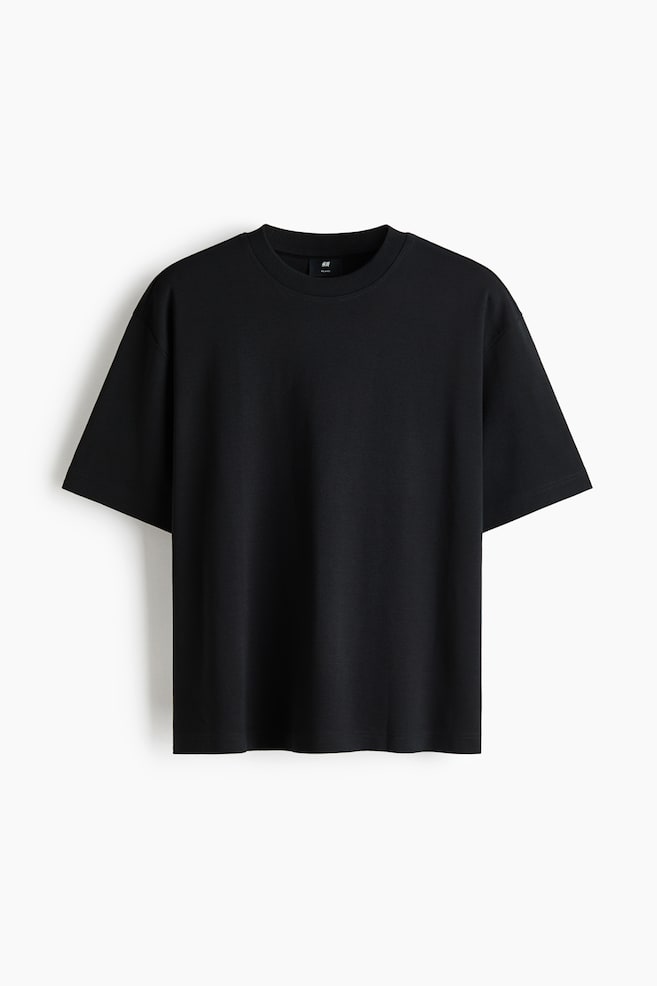 A black T-shirt is facing front, featuring a ribbed crew neck and short sleeves with dropped shoulders. It showcases a relaxed, oversized fit, and a small black H&M size tag is visible on the inner back collar. - 1