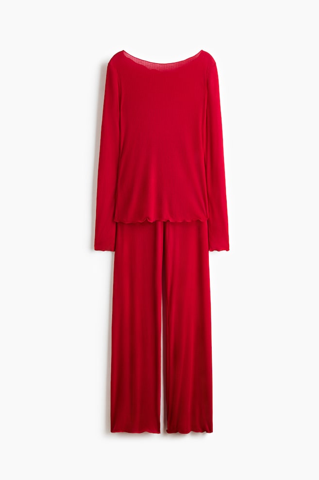 Ein rotes Pyjama-Set aus Rippjersey hÃ¤ngt frontal ausgerichtet und besteht aus einem langÃ¤rmeligen Oberteil mit U-Boot-Ausschnitt sowie einer dazu passenden Hose mit weitem Bein. Beide Teile sind mit OverlocknÃ¤hten und Lettuce-SaumabschlÃ¼ssen versehen. - 1