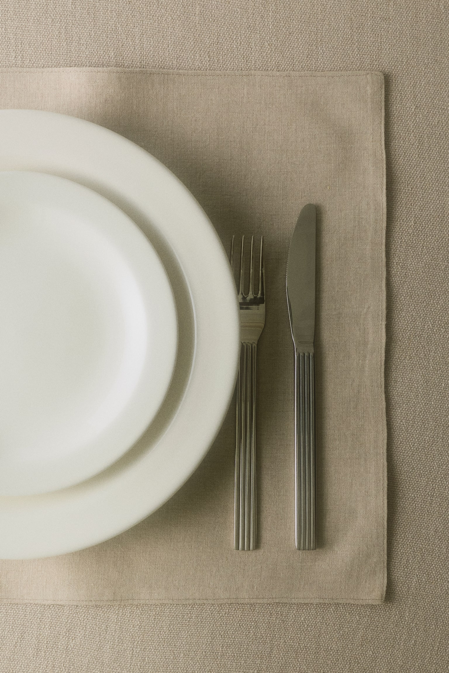 Suorakulmainen pöytäliina, jossa on luonnollinen beige väri ja näkyvä pellavamainen kudos. Se on asetettu tasaisesti, ja sen vasemmalla puolella kulkee näkyvä pystysauma. - 1
