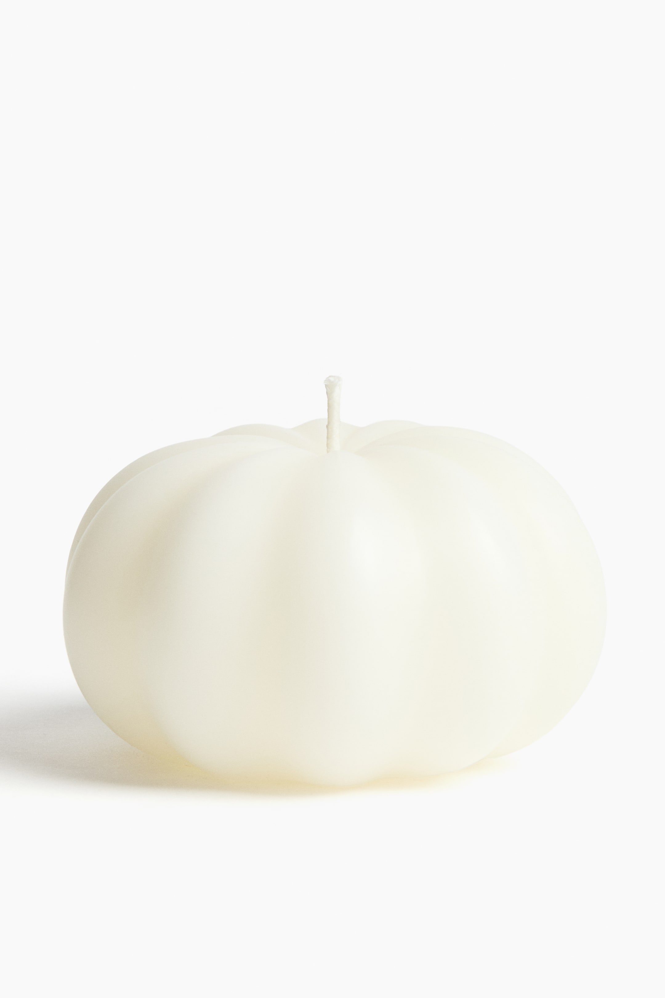 View larger image: The off-white, pumpkin-shaped candle is facing forward, with distinct vertical ridges around its body, and a short white wick protruding from the center of the top.