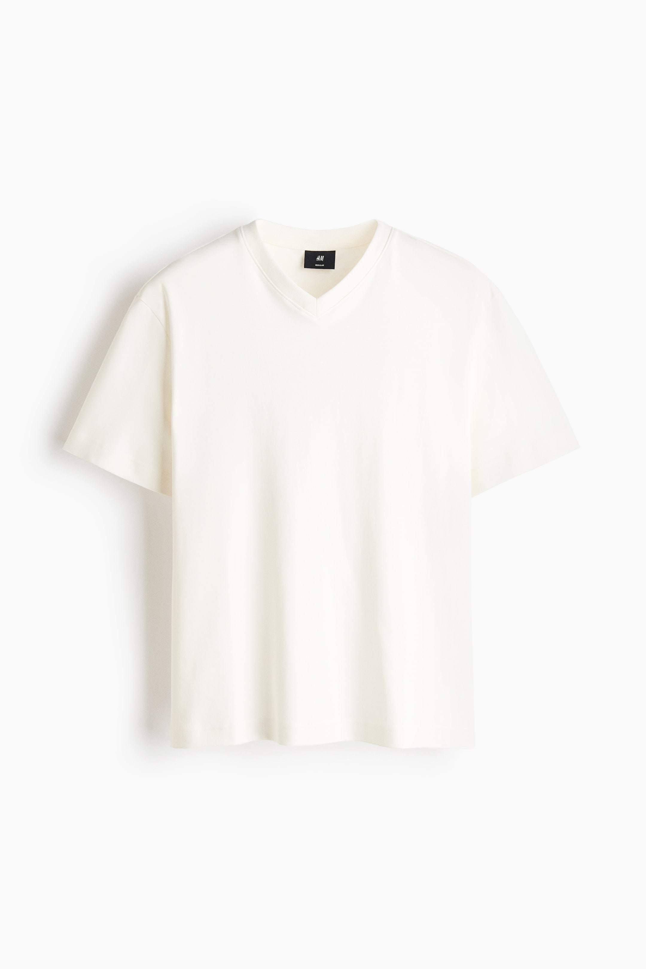 View larger image: A cream V-neck T-shirt is being shown from the front, featuring short sleeves, a relaxed fit, and a black tag visible at the back of the neck.