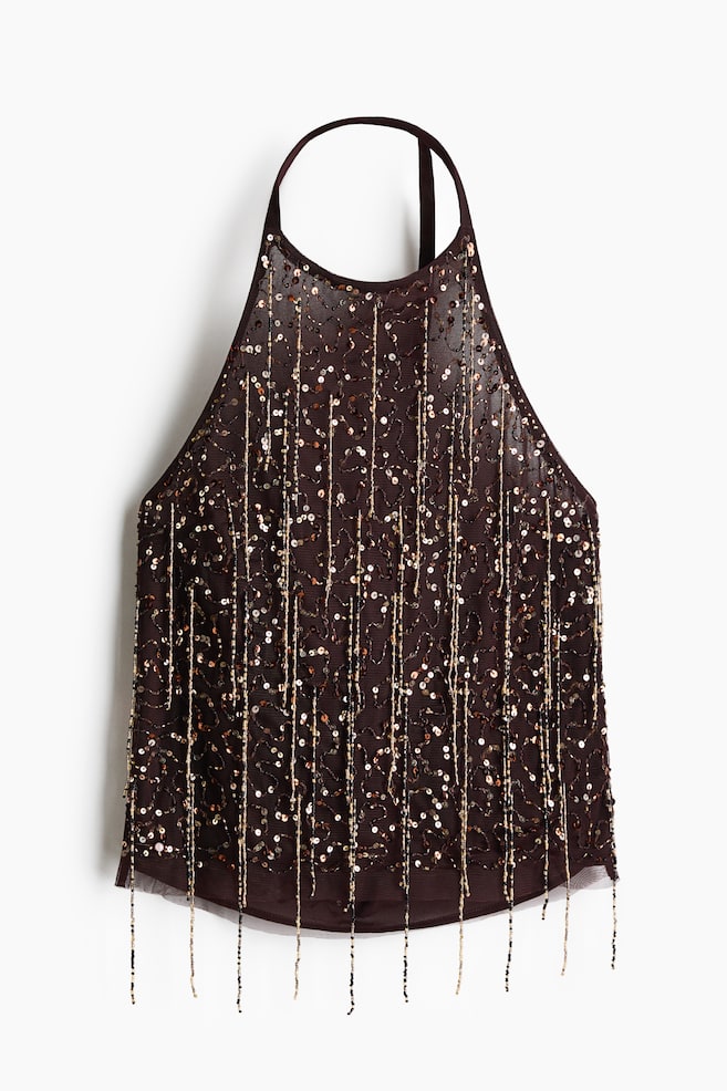 A dark brown halter top is shown from the front, featuring a sheer mesh overlay embellished with all-over shimmering bronze sequins and long, beaded strands draping past the gently rounded hem. The top is designed with a high halter neckline, thin straps, and a solid lining beneath the sheer outer layer. - 1