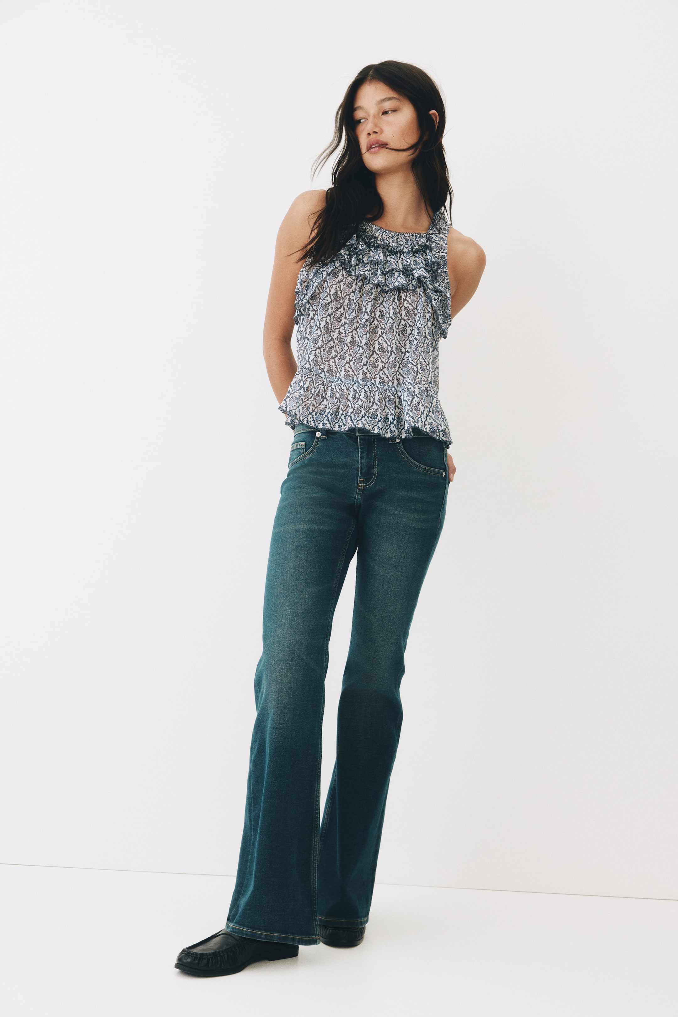 View larger image: Dark wash denim jeans, featuring a low waist, a button closure, and faux front pockets, are being worn by the model. The jeans are fitted slim through the thigh, flaring from the knee, and extending to cover the top of the feet.