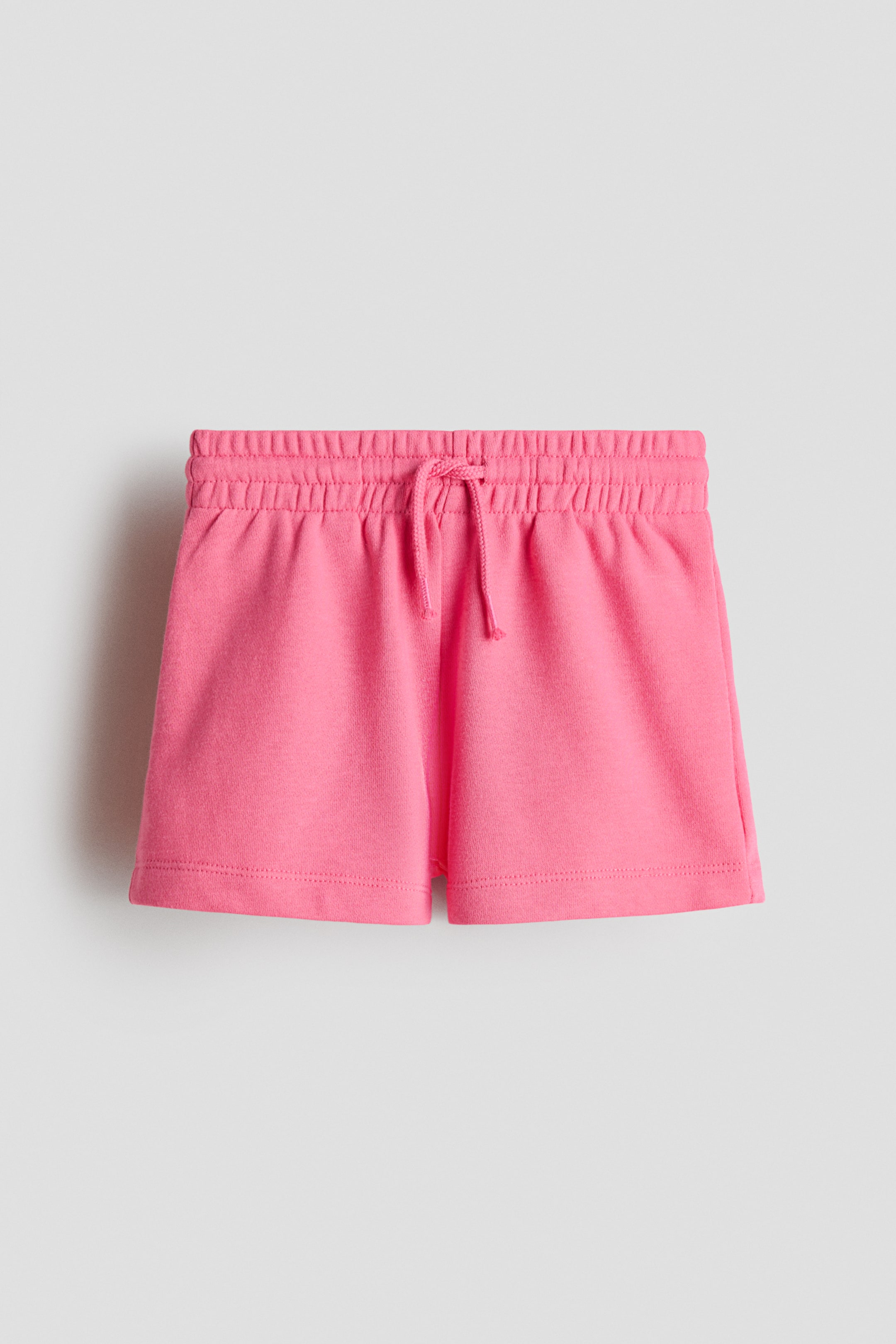 View larger image: Pink shorts are presented flat, facing front. They feature an elastic waistband with a drawstring tie at the center front, and are made from a lightweight sweatshirt fabric.