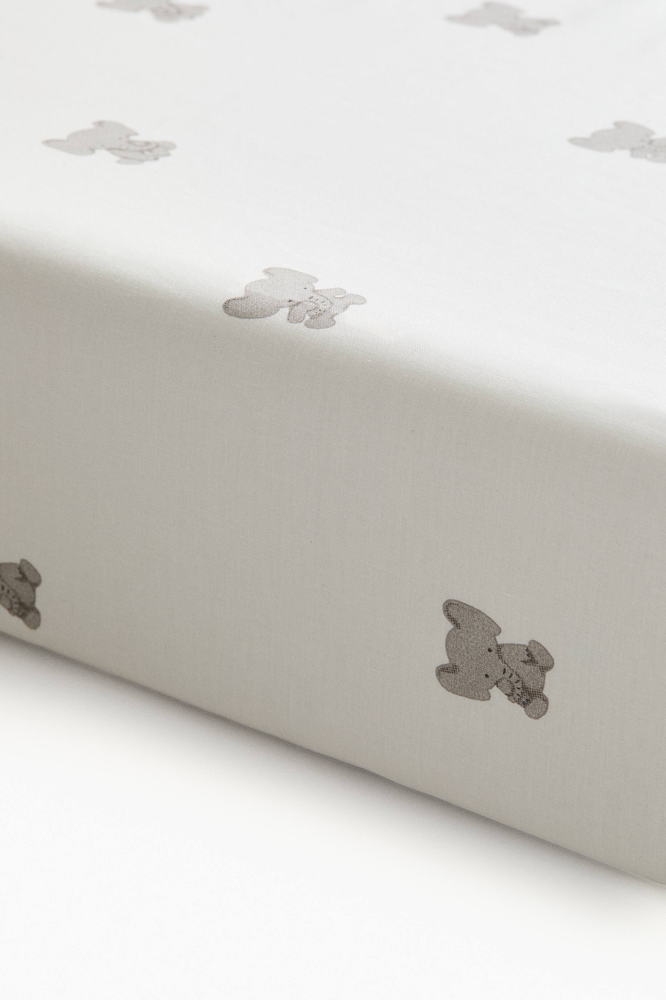 View larger image: A light cream-colored fitted sheet features a repeating pattern of small, gray printed teddy bears. The sheet stretches smoothly over a mattress corner, showcasing its neat fit and soft fabric texture.