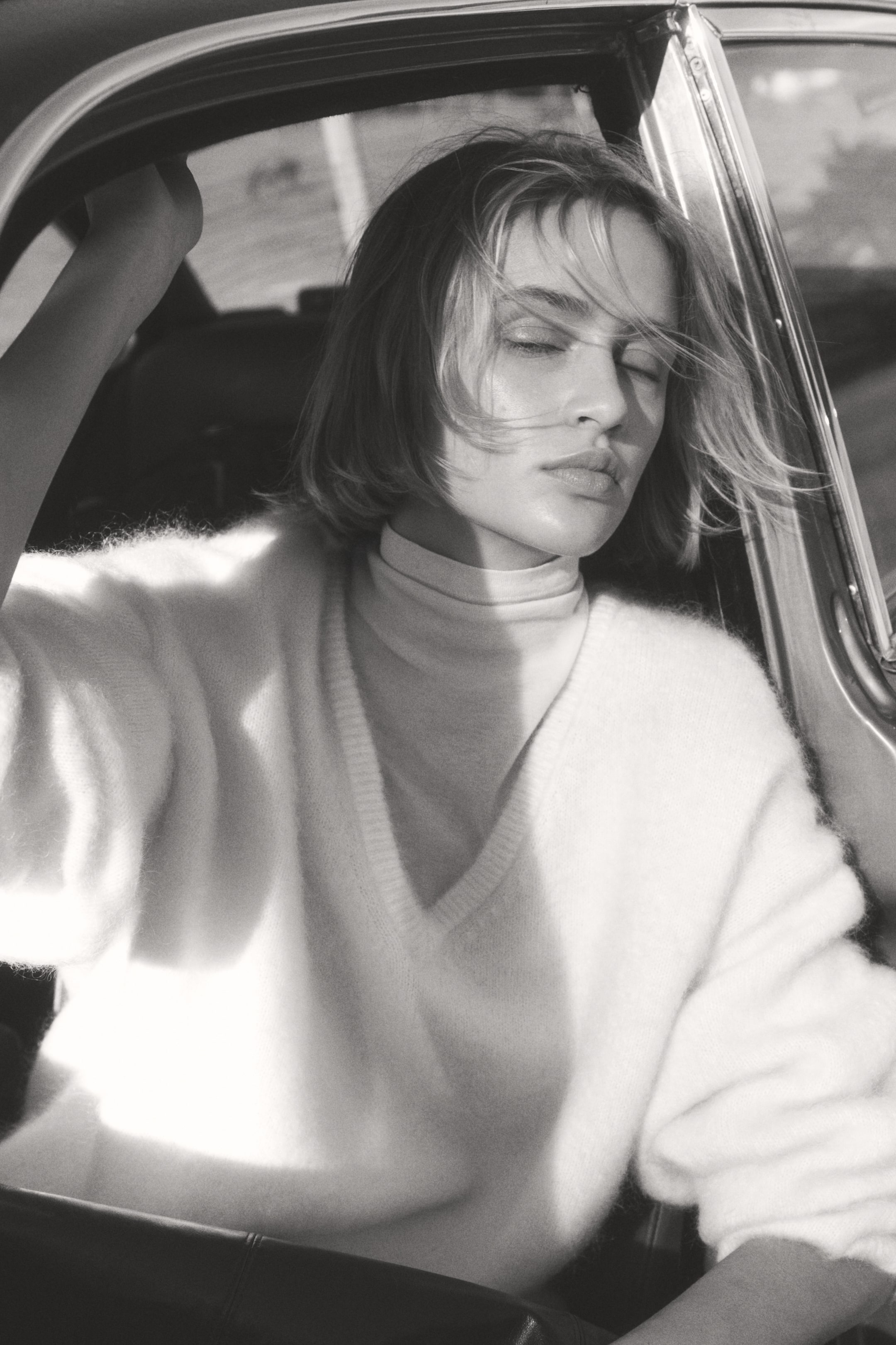 Grösseres Bild ansehen: Ein flauschiger, hellfarbener V-Ausschnitt-Pullover wird getragen, über einem passenden hellfarbenen Rollkragenpullover geschichtet. Sein lockerer Schnitt und die langen Ärmel sind sichtbar, wobei der V-Ausschnitt aus einer frontalen, leicht geneigten Perspektive präsentiert wird.