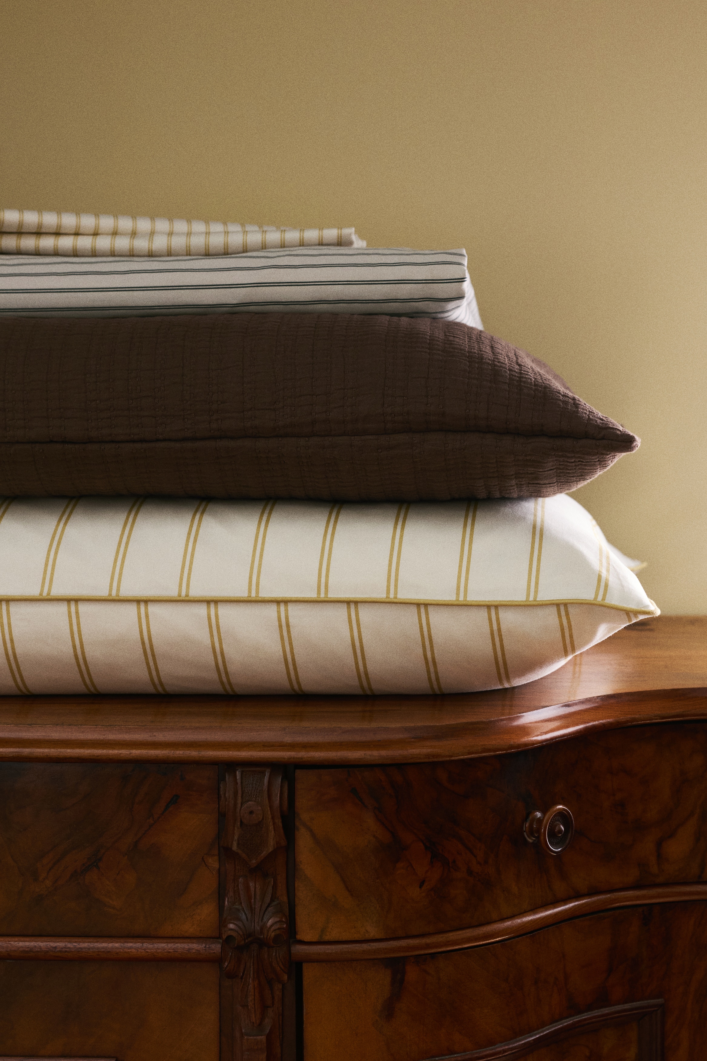 Une housse de coussin rectangulaire marron est orientée vers l'avant, affichant un tissage en coton doux et froissé. Elle est détaillée avec des coutures pour une texture supplémentaire.