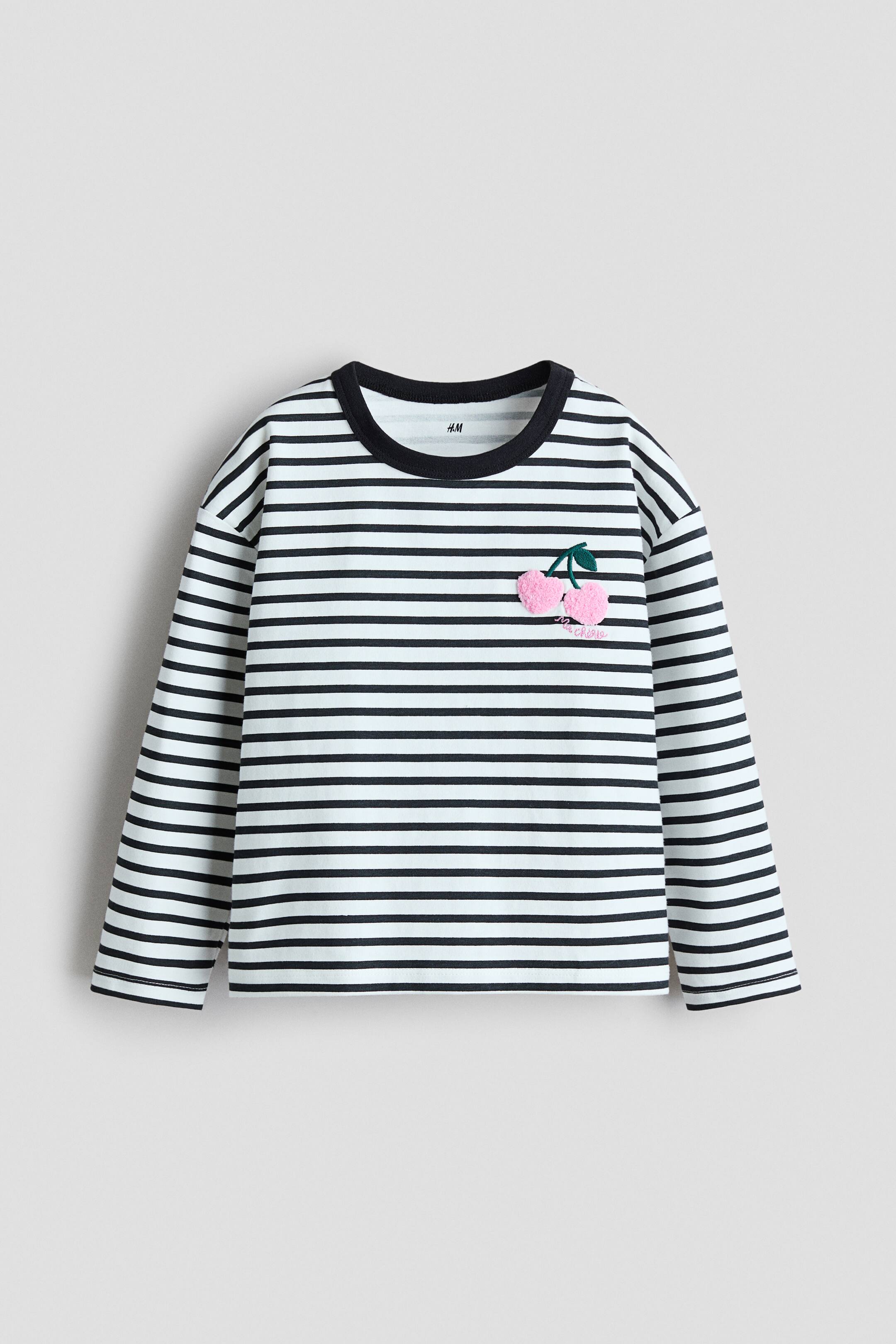 View larger image: A long-sleeved, white and black striped top is facing front. It features a black crew neck and a pink textured cherry appliqué with green leaves on the upper left chest, with the word "cherries" embroidered in white below it.