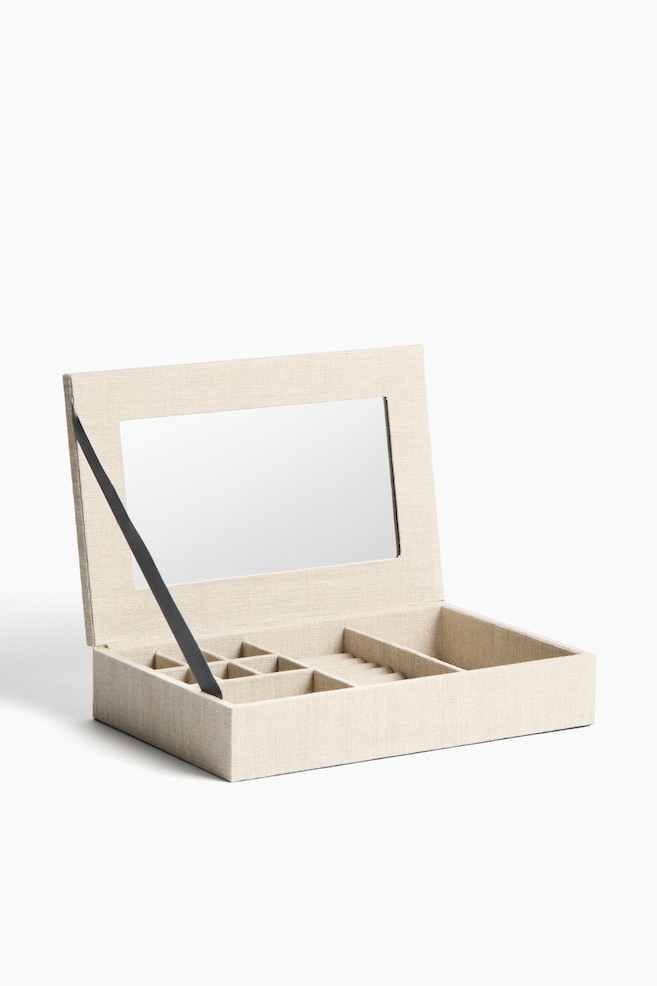 A beige fabric jewellery box opens towards the front. Its lid features a rectangular mirror, with a black ribbon supporting the lid. The box's interior displays multiple compartments and ring rolls. - 1