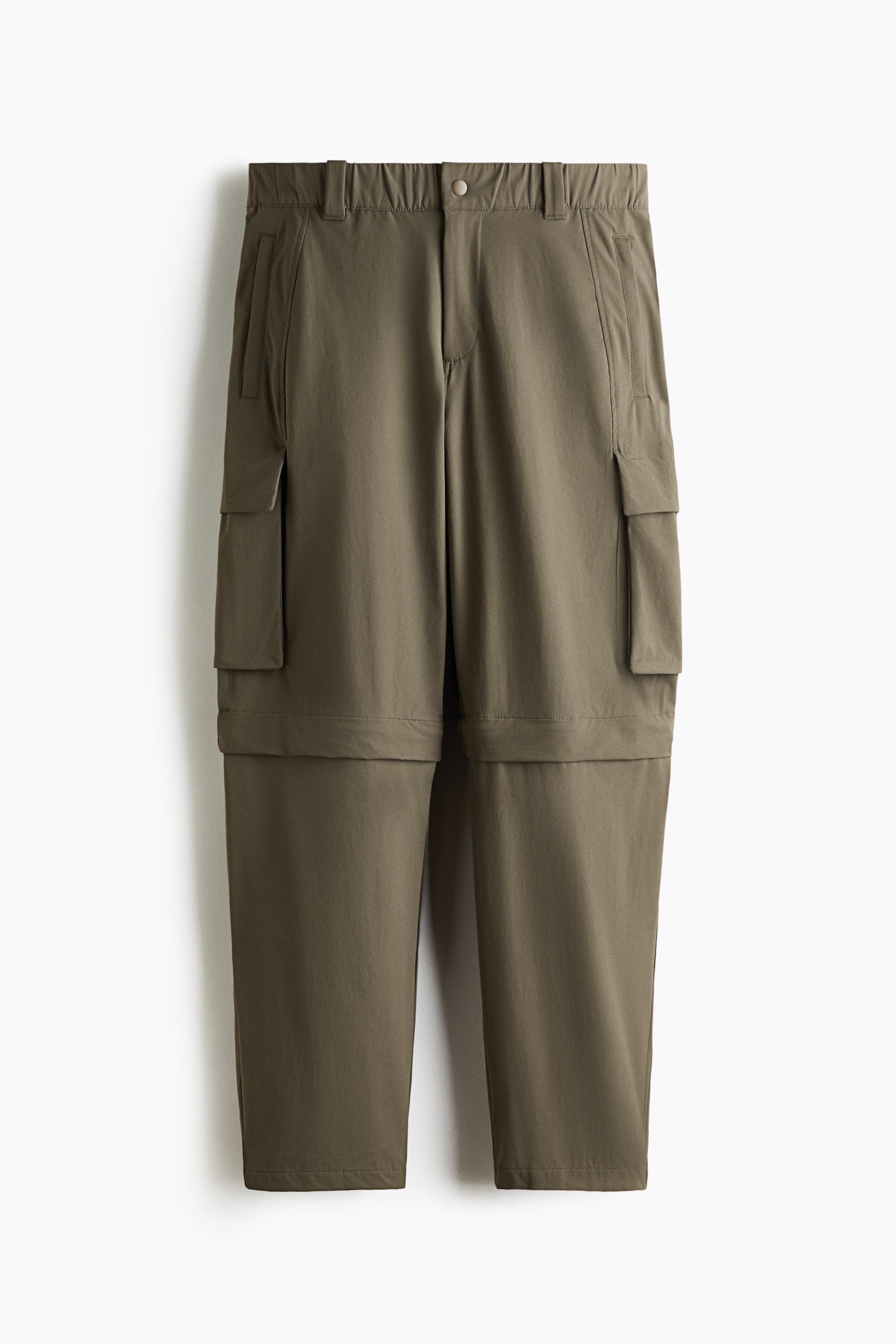 View larger image: The olive green convertible cargo trousers are showcasing a front view, featuring an elasticised waistband with belt loops and a snap button closure. Large flap cargo pockets are visible on both thighs, and a horizontal zip is encircling each leg, indicating their convertible design.