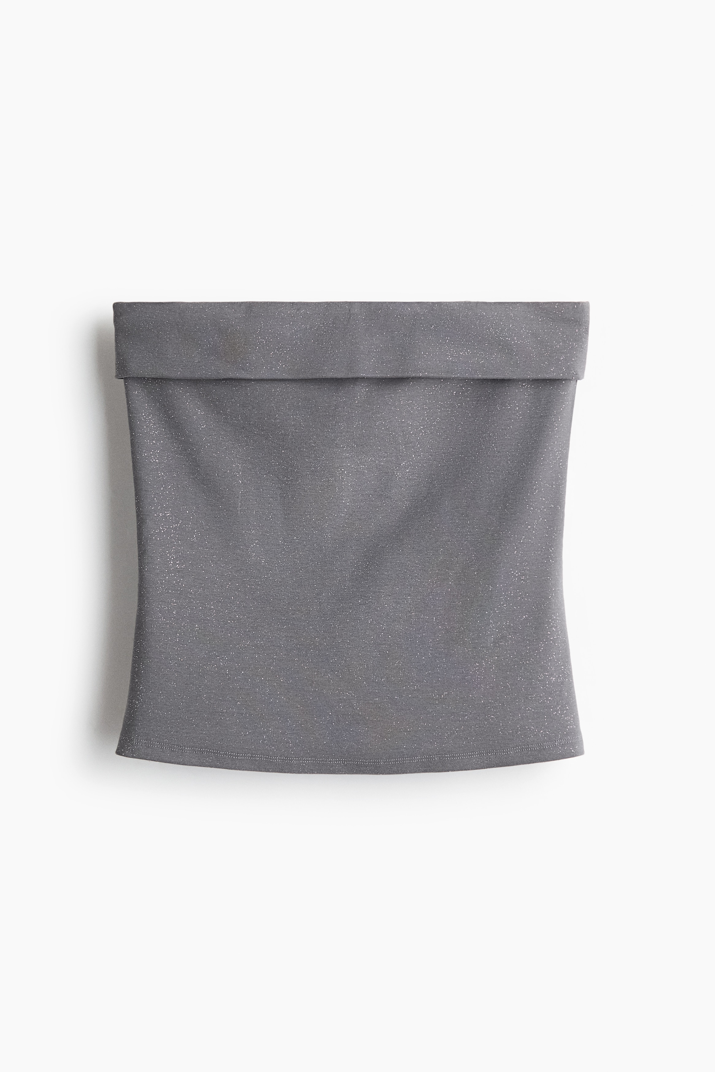 Modelka má na sobě třpytivý šedý přiléhavý bandeau top s ohrnutým horním okrajem. Top je stylizovaný se širokými černými džínami a černým páskem.