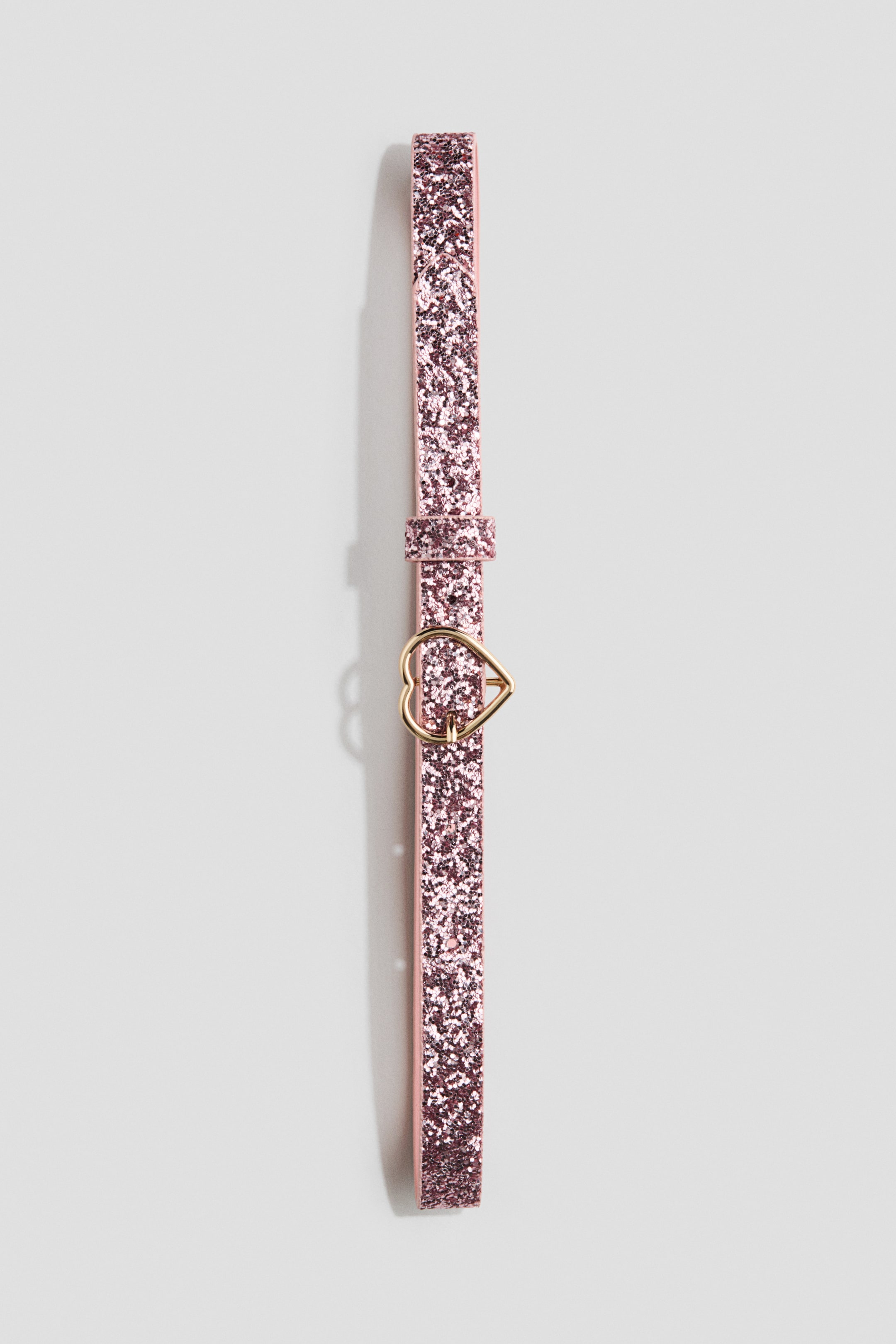 Voir une image plus grande: Une ceinture rose avec une finition scintillante est dotée d'une boucle en métal doré en forme de cœur. La ceinture est présentée verticalement, mettant en valeur son design avant.