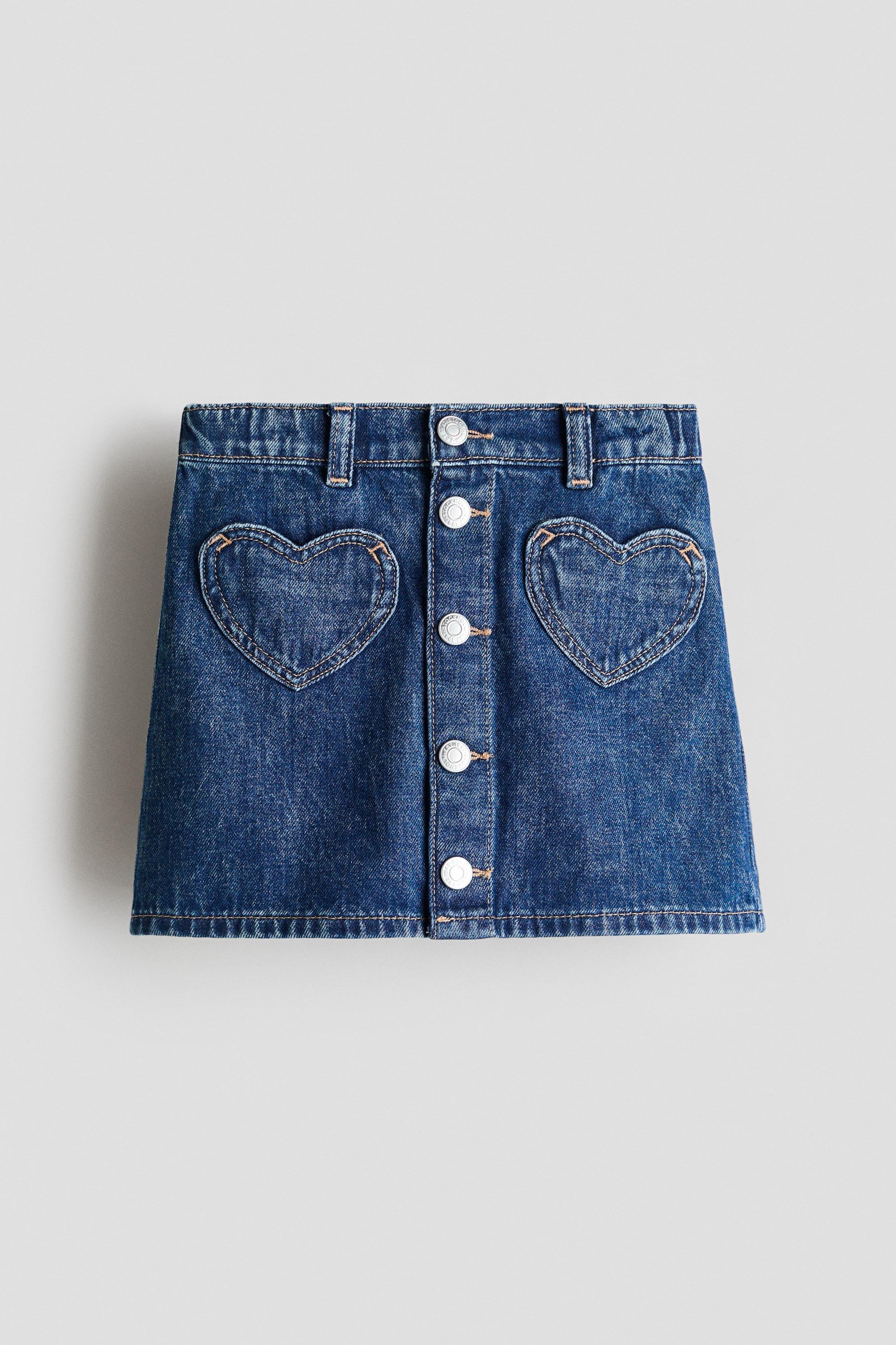 Größeres Bild ansehen: Ein A-Linien-Rock aus dunkelblauem Baumwoll-Denim präsentiert seine Vorderseite mit herzförmigen Aufsatztaschen und einer Reihe von silbernen Druckknöpfen in der Mitte.
