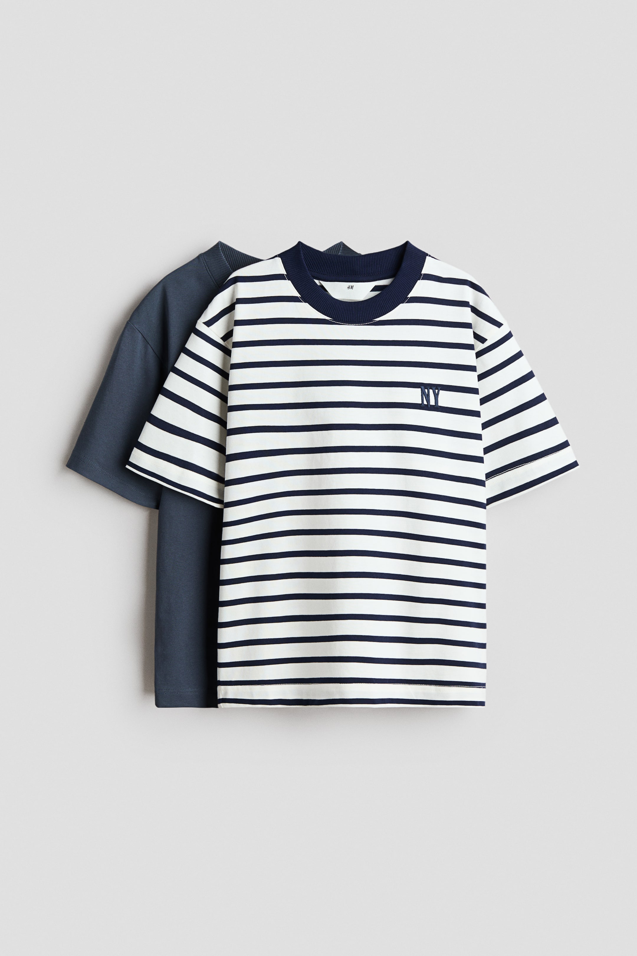 Agrandir l'image: Deux t-shirts sont posés à plat : un t-shirt rayé blanc et bleu marine arborant un 'NY' brodé sur la poitrine gauche et un col rond côtelé bleu marine, couvrant partiellement un t-shirt uni bleu foncé.