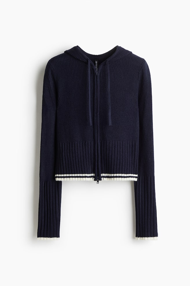 A short, fitted dark blue ribbed knit cardigan is facing front. It is featuring a drawstring hood, a two-way zipper running down the front, and wide, white and dark blue striped ribbed trim detailing the cuffs and hem. - 1