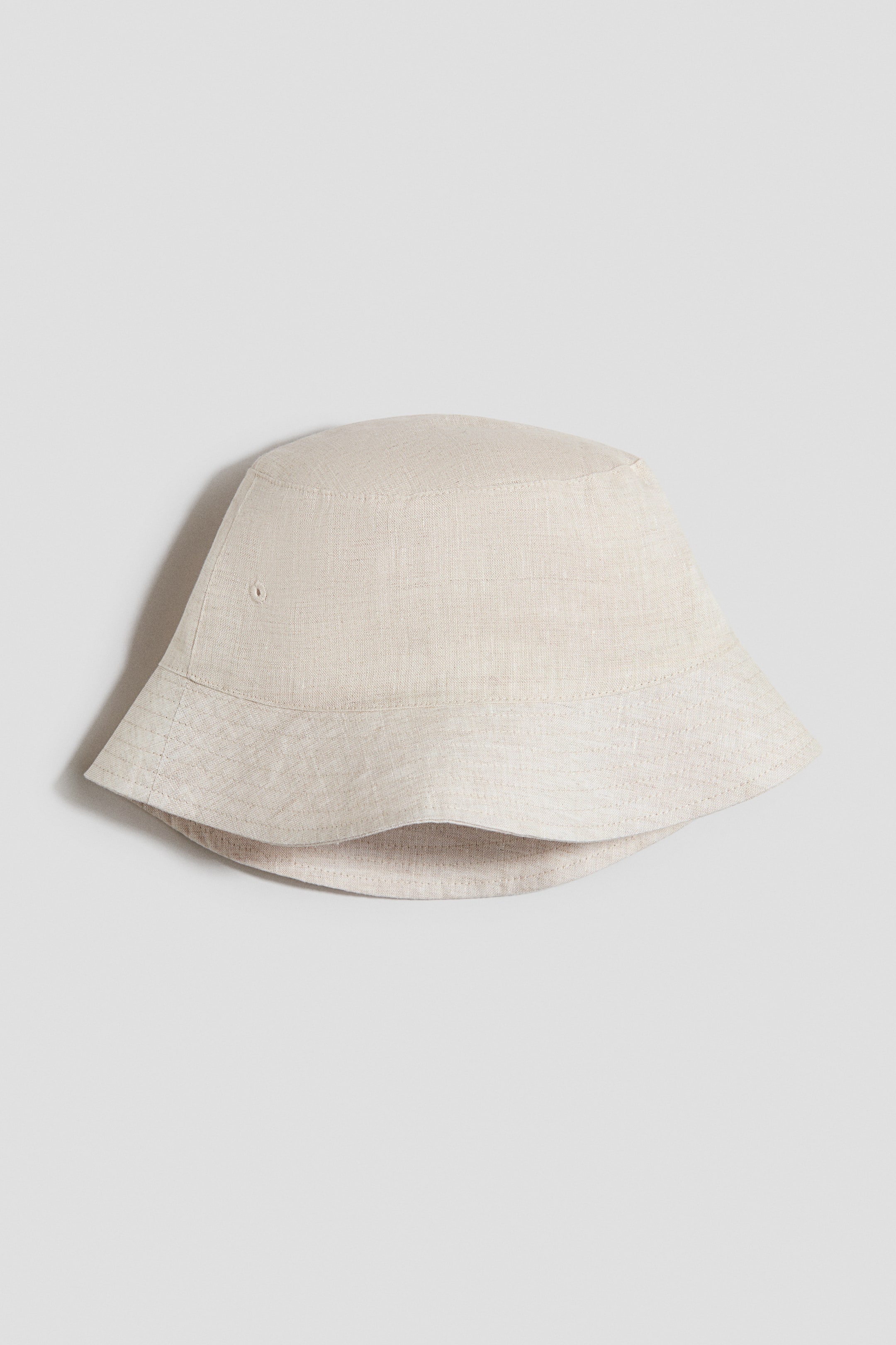 Ampliar la imagen: Un bucket hat de mezcla de lino en beige claro presenta su vista frontal, con una cima plana, una corona suavemente inclinada con un pequeño ojal de ventilación y un ala ancha que se inclina hacia abajo con costuras visibles.