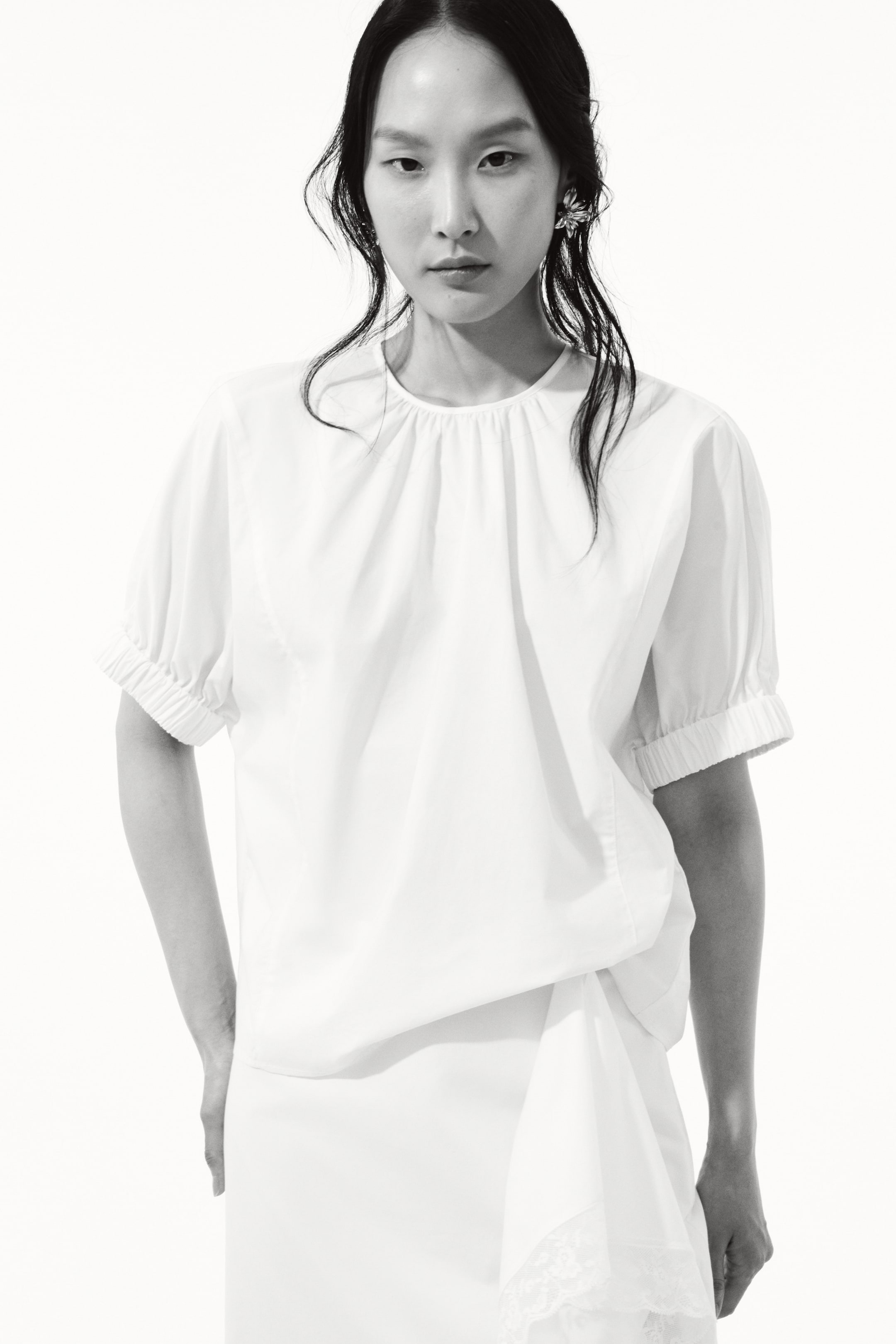 View larger image: "The model is wearing a white blouse with a gathered round neckline and short puffed sleeves with elasticated cuffs. It's paired with a white skirt that features a lace trim."