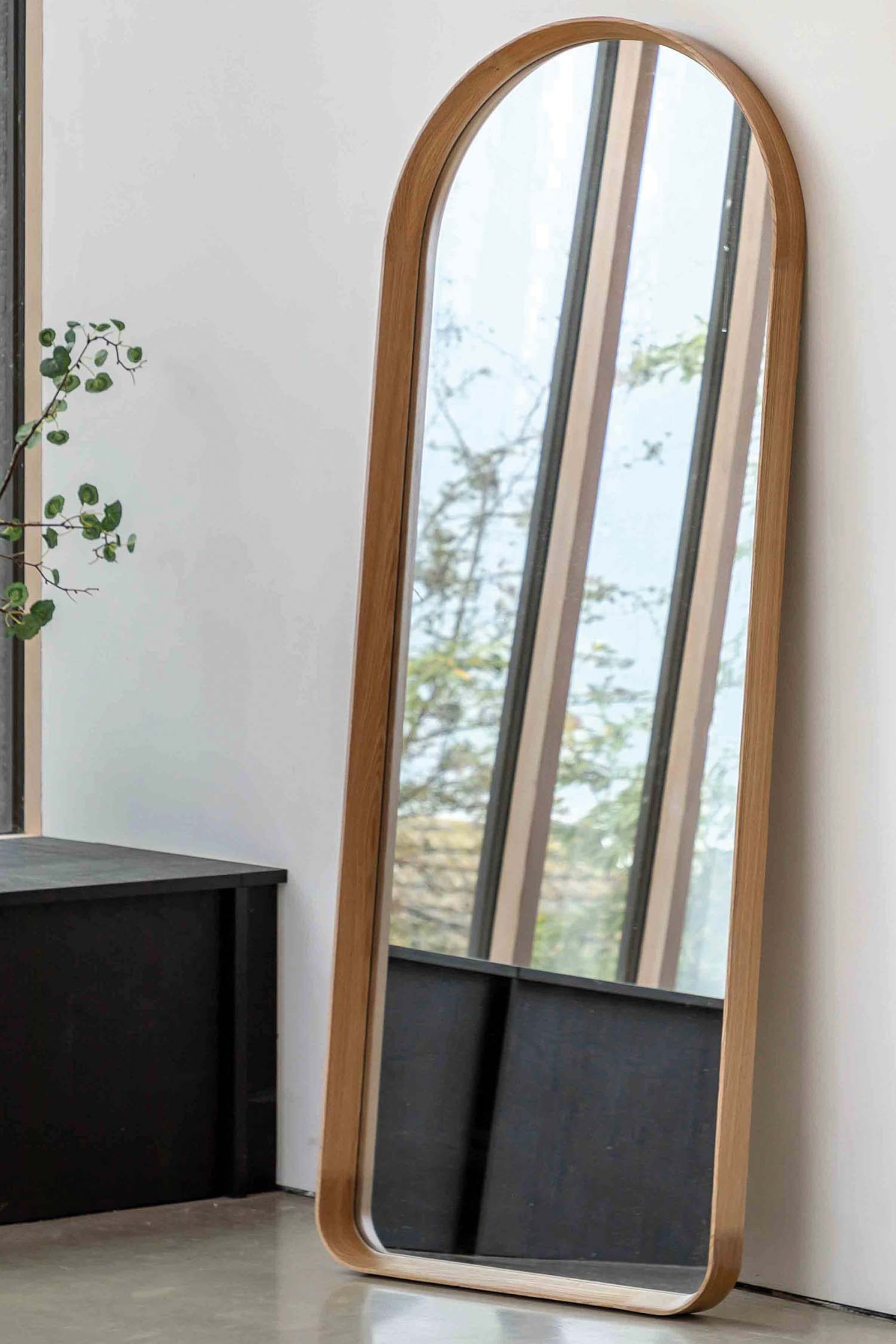 View larger image: An arch-top full-length mirror is standing, leaning slightly backwards. It features a light natural wood frame with visible grain and smoothly rounded edges.