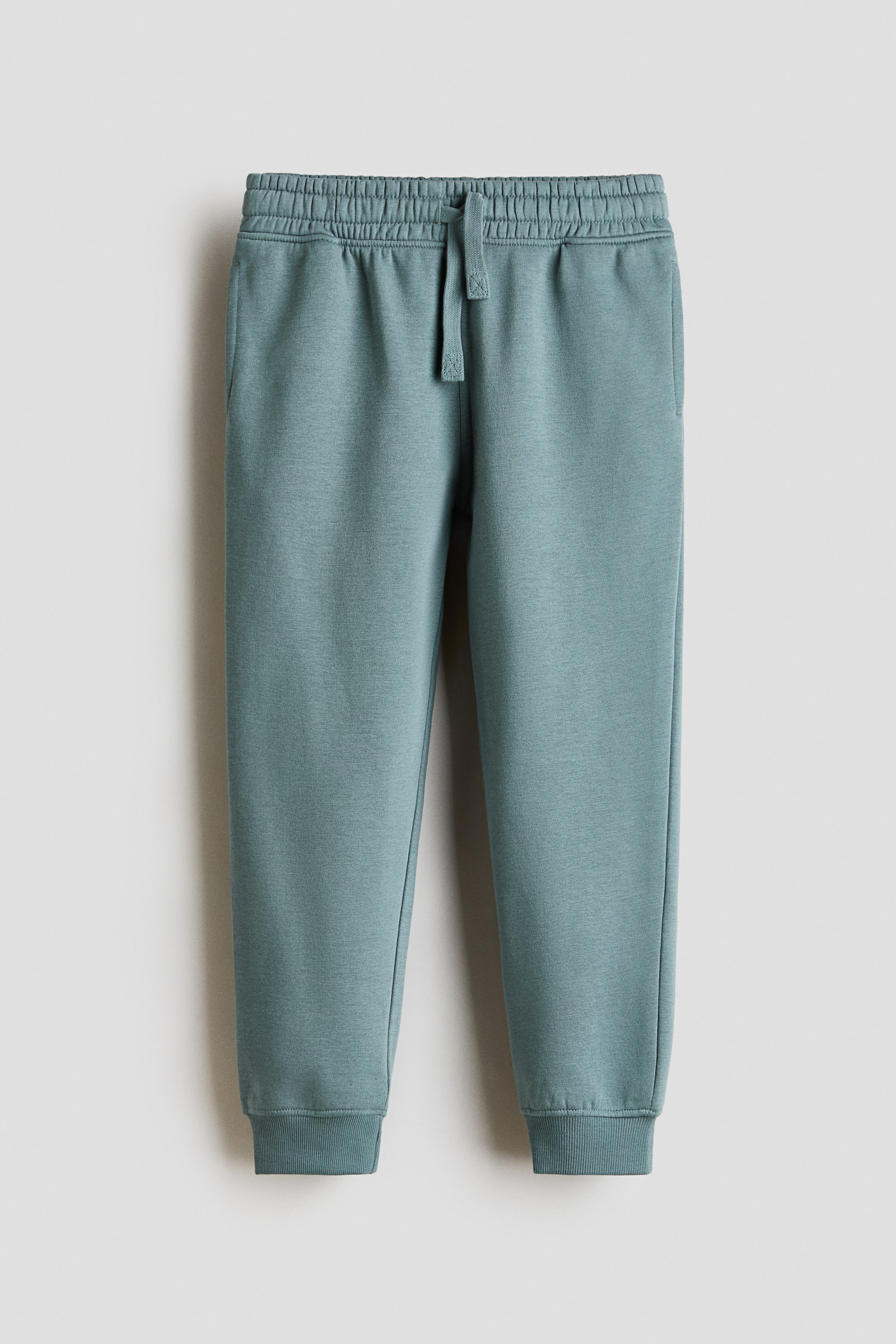 View larger image: Front-facing sweatpants feature an elastic waistband with a visible drawstring, side pockets, and ribbed cuffs, all in a solid teal-green knit fabric.