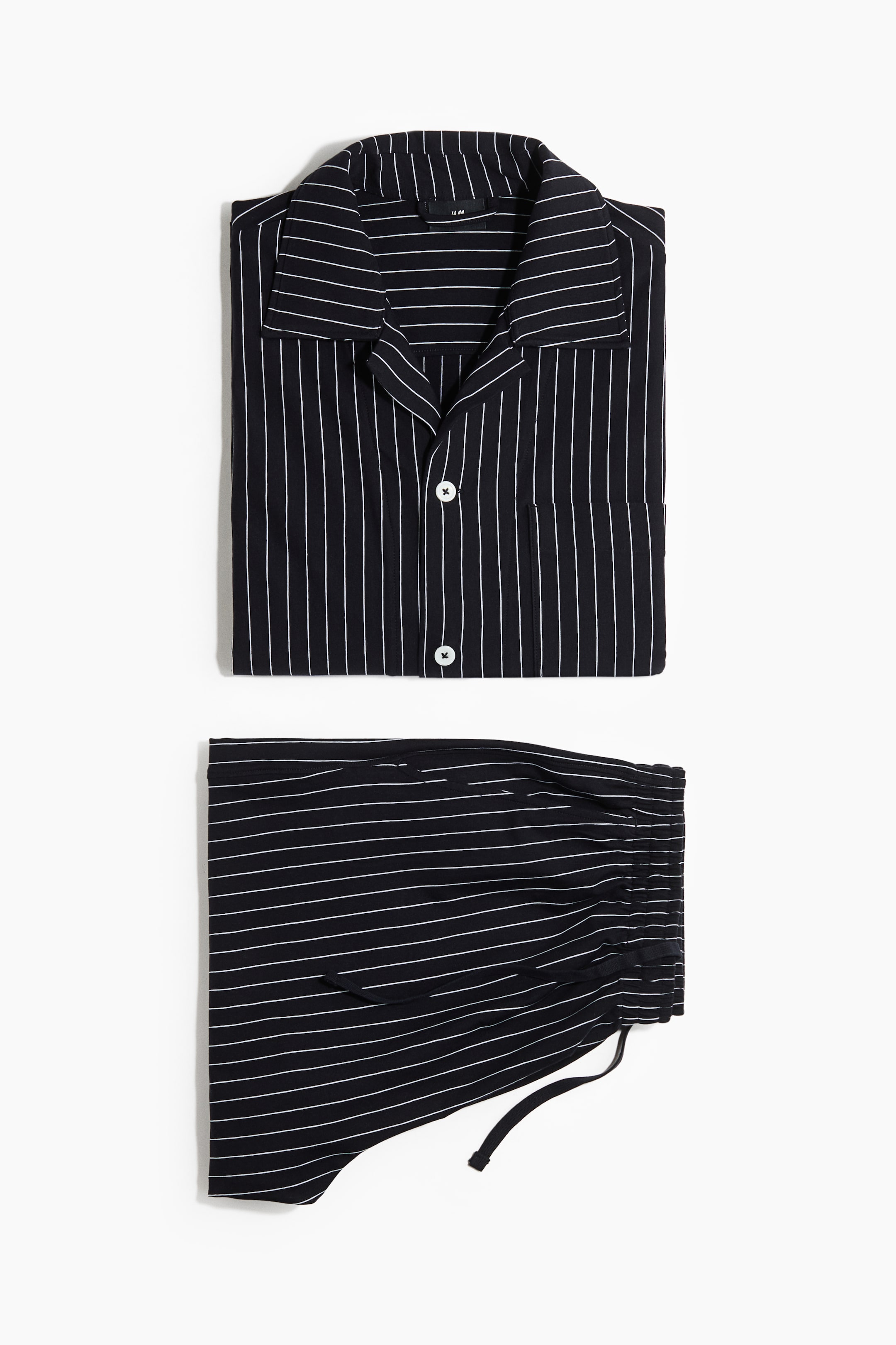View larger image: A black and white pinstriped pajama set is laid flat, facing front. The top features vertical white stripes, a revere collar, two white buttons on the front placket, and a chest pocket. The matching bottom displays horizontal white stripes and a drawstring elasticated waist.