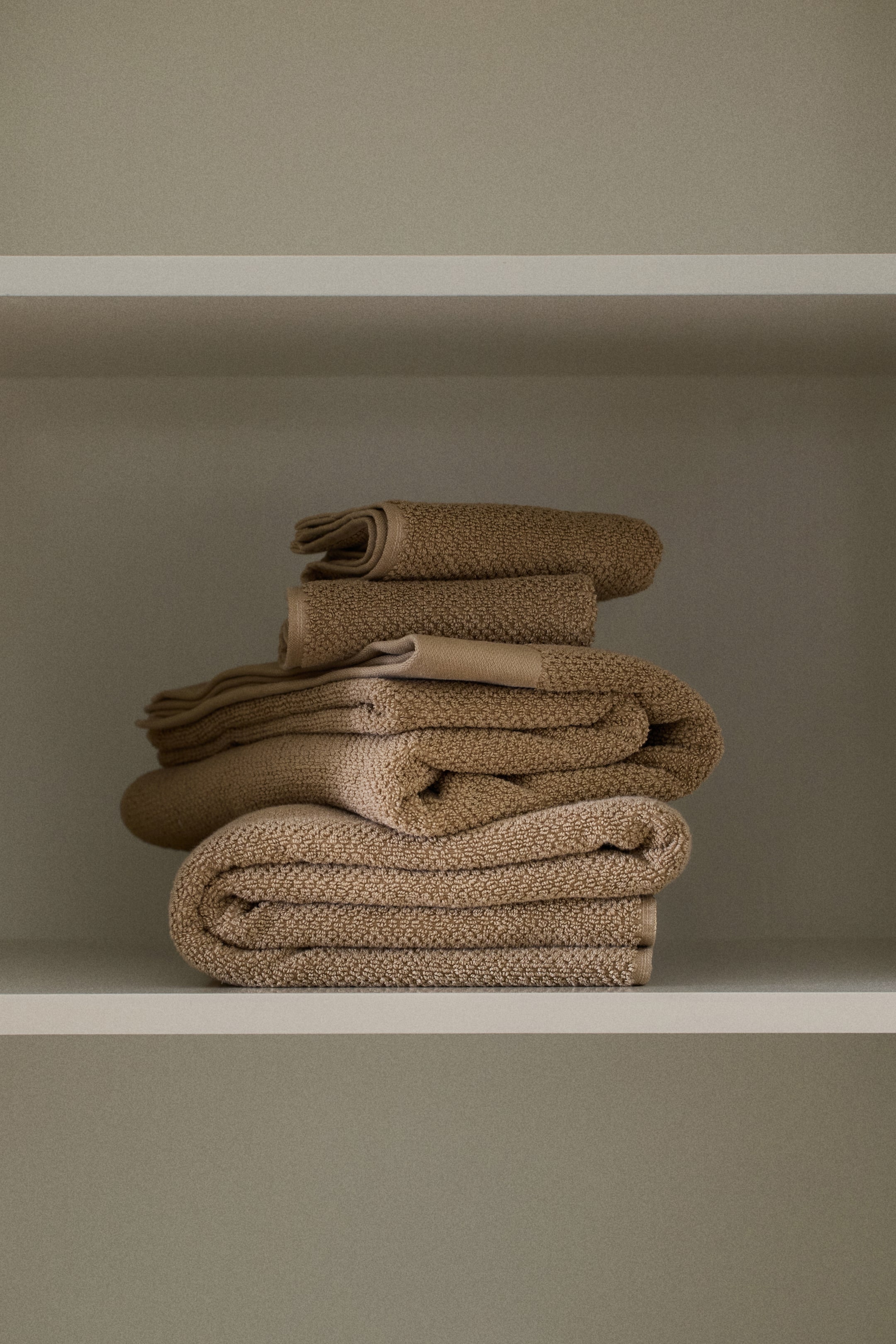 View larger image: A stack of classic bath towels showcases its soft, looped cotton terry texture in a light brown colour. The neatly folded stack features multiple towels of varying sizes.