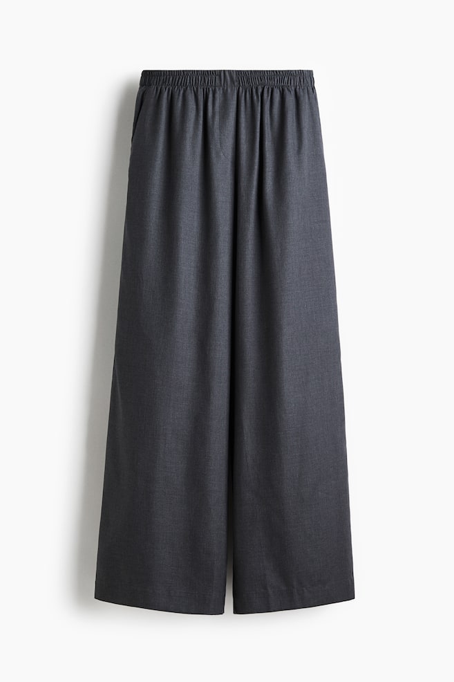 A pair of dark gray, wide-leg pants is being presented from the front, featuring an elasticated waistband and side seam pockets. - 1