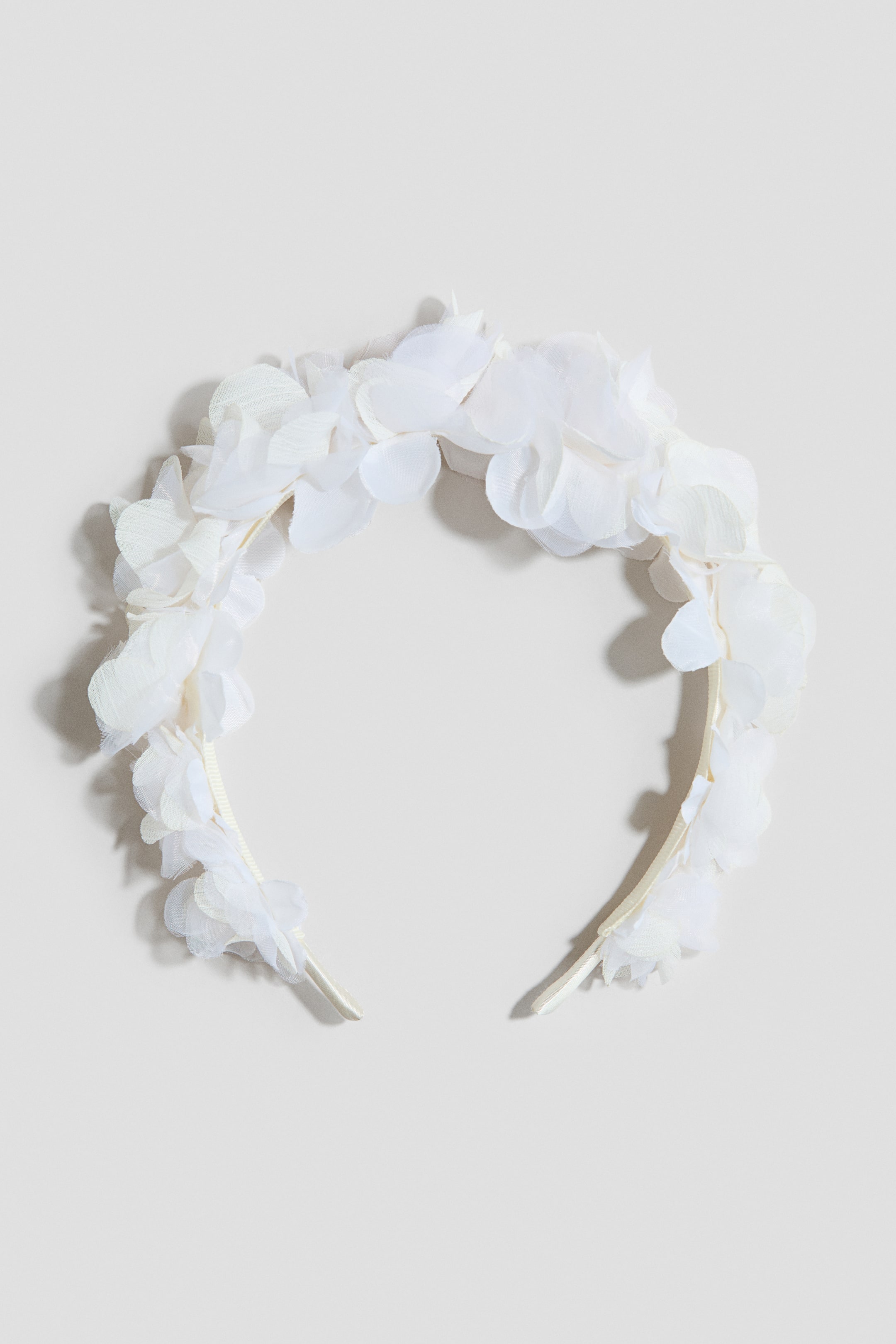 Agrandir l'image: Un bandeau floral blanc est positionné à l'AVANT, présentant de nombreuses fleurs en tissu transparent superposées, s'assemblant densément le long de sa courbe supérieure, avec une bande étroite enveloppée de tissu formant sa base.
