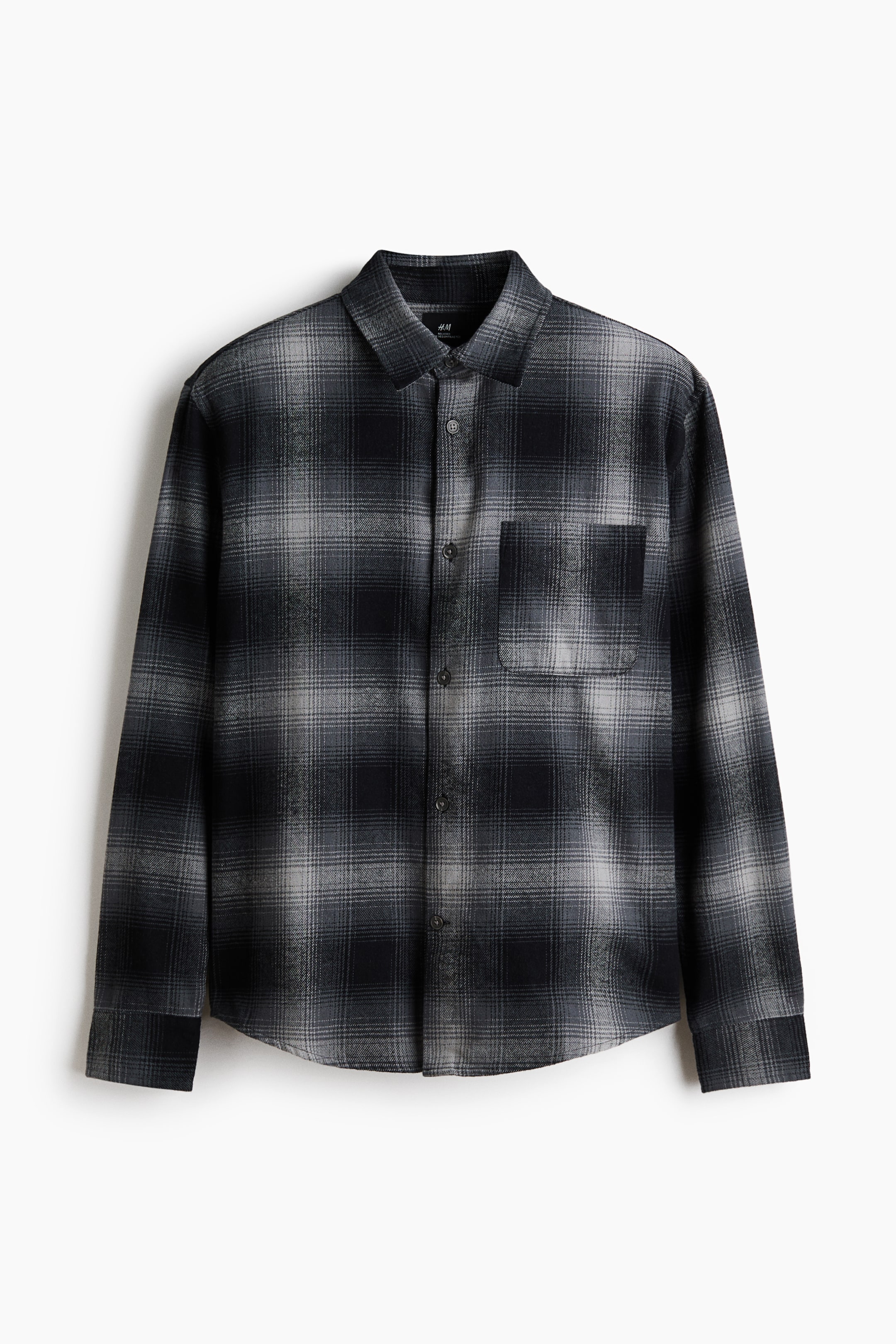 View larger image: A black and grey plaid flannel shirt is shown from the front, featuring a turn-down collar, a French front, and an open chest pocket on the left side. Long sleeves with buttoned cuffs and sleeve plackets extend from the body, and the shirt finishes with a gently rounded hem, indicating a loose fit.