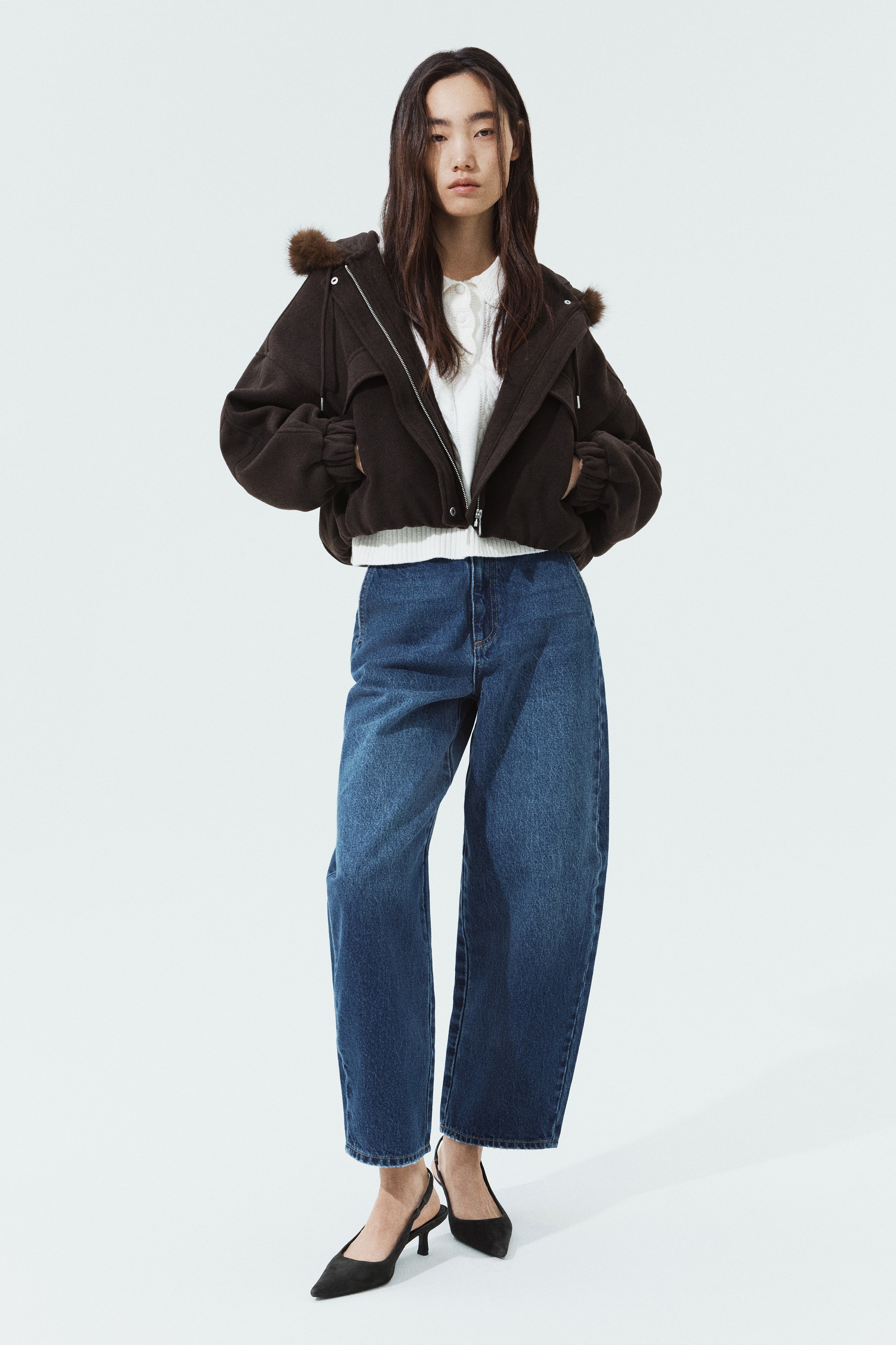 This pair of high-waisted, barrel-leg blue jeans is shown from the front, featuring a medium-blue wash with subtle fading on the thighs. The jeans feature slanted side pockets, a zip fly with a button closure, and a gold-tone chain detail woven through the front belt loops.