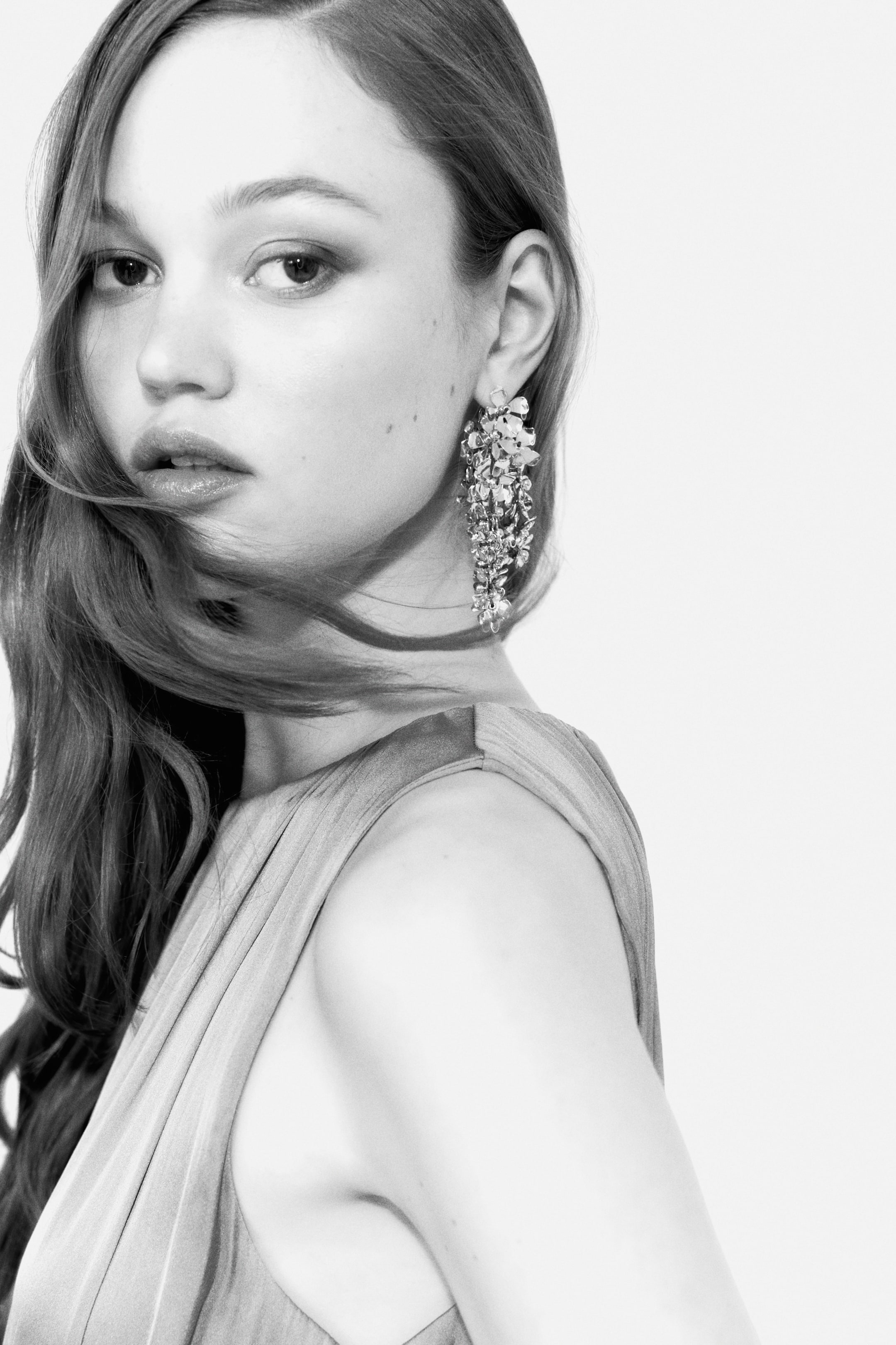 View larger image: The earring is a long, chandelier style, showcasing multiple irregularly shaped, reflective elements that are grouped together and cascading downwards from the ear.