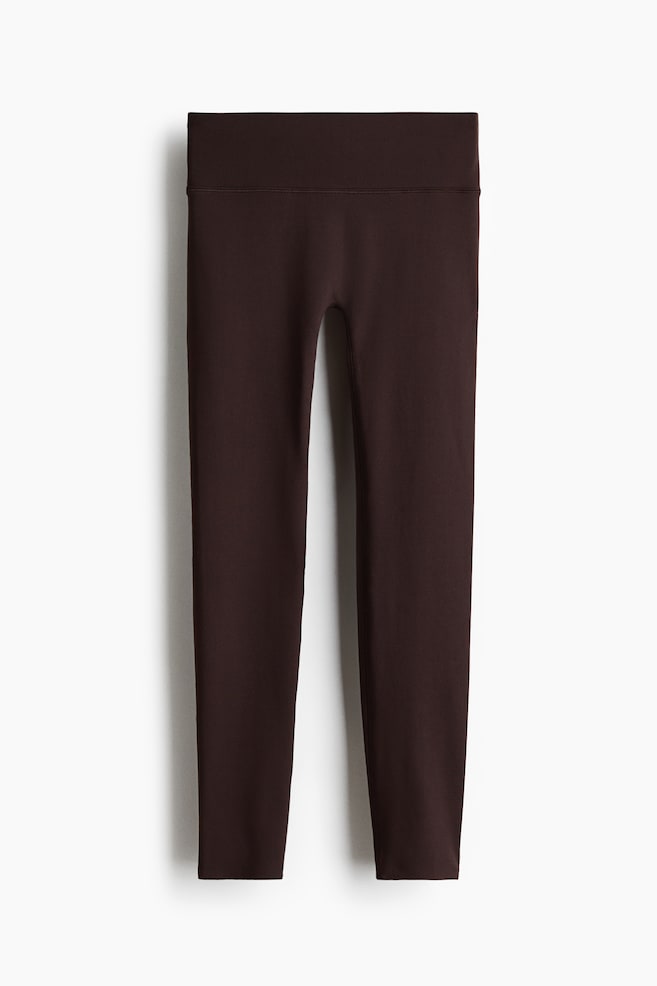 Dark brown sports leggings are displaying a wide, high-rise waistband. They are featuring a smooth, fitted silhouette with minimal visible seams and a full-length design, presented from the front. - 1