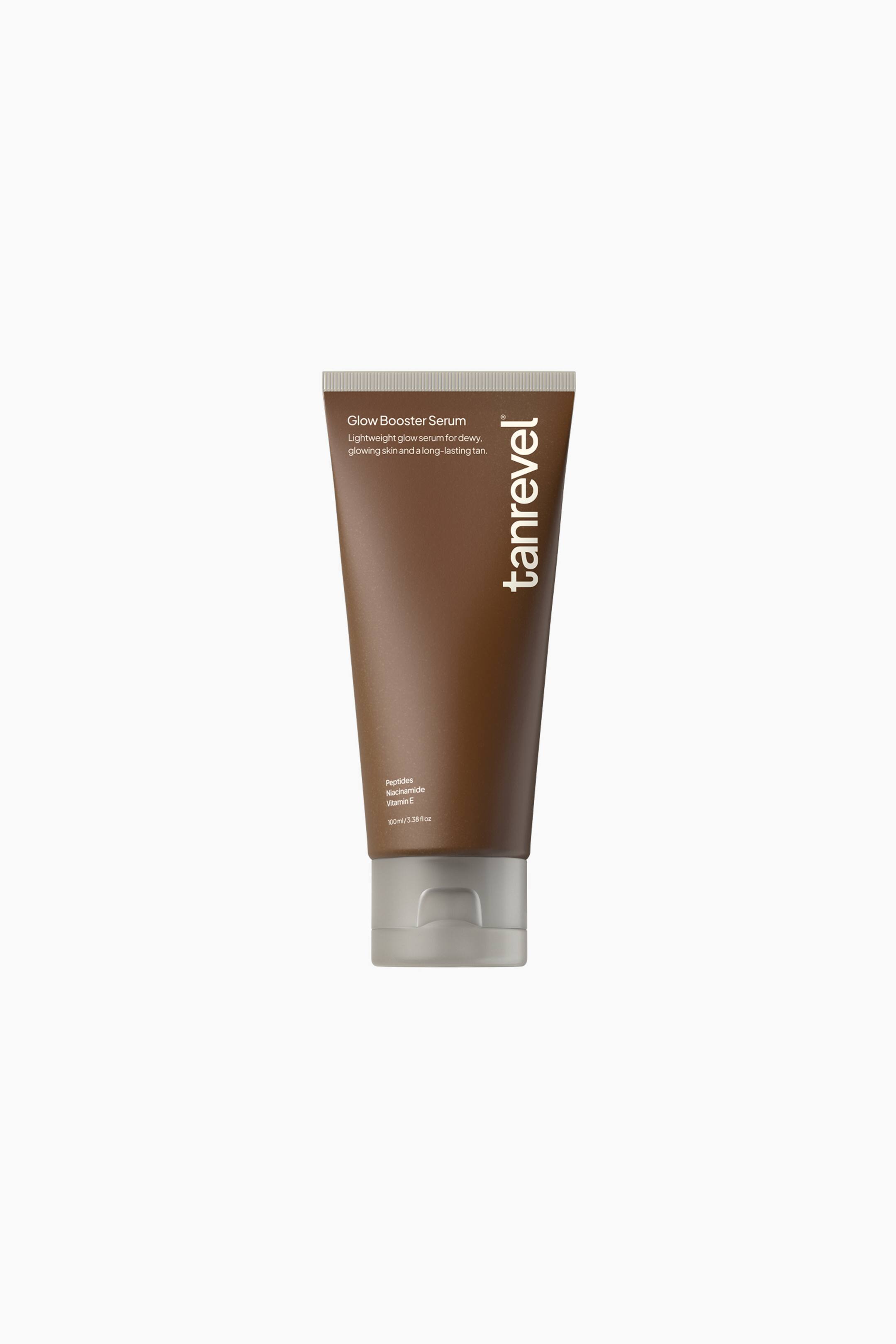 Se større billede: Glow Booster Serum står oprejst og præsenteres i en mat brun squeeze-tube med en kontrasterende grå flip-top-hætte ved bunden. Den frontvendte tube viser hvid tekst med produktnavnet, nøgleingredienserne og det lodrette "tanrevel"-brandnavn langs højre kant.