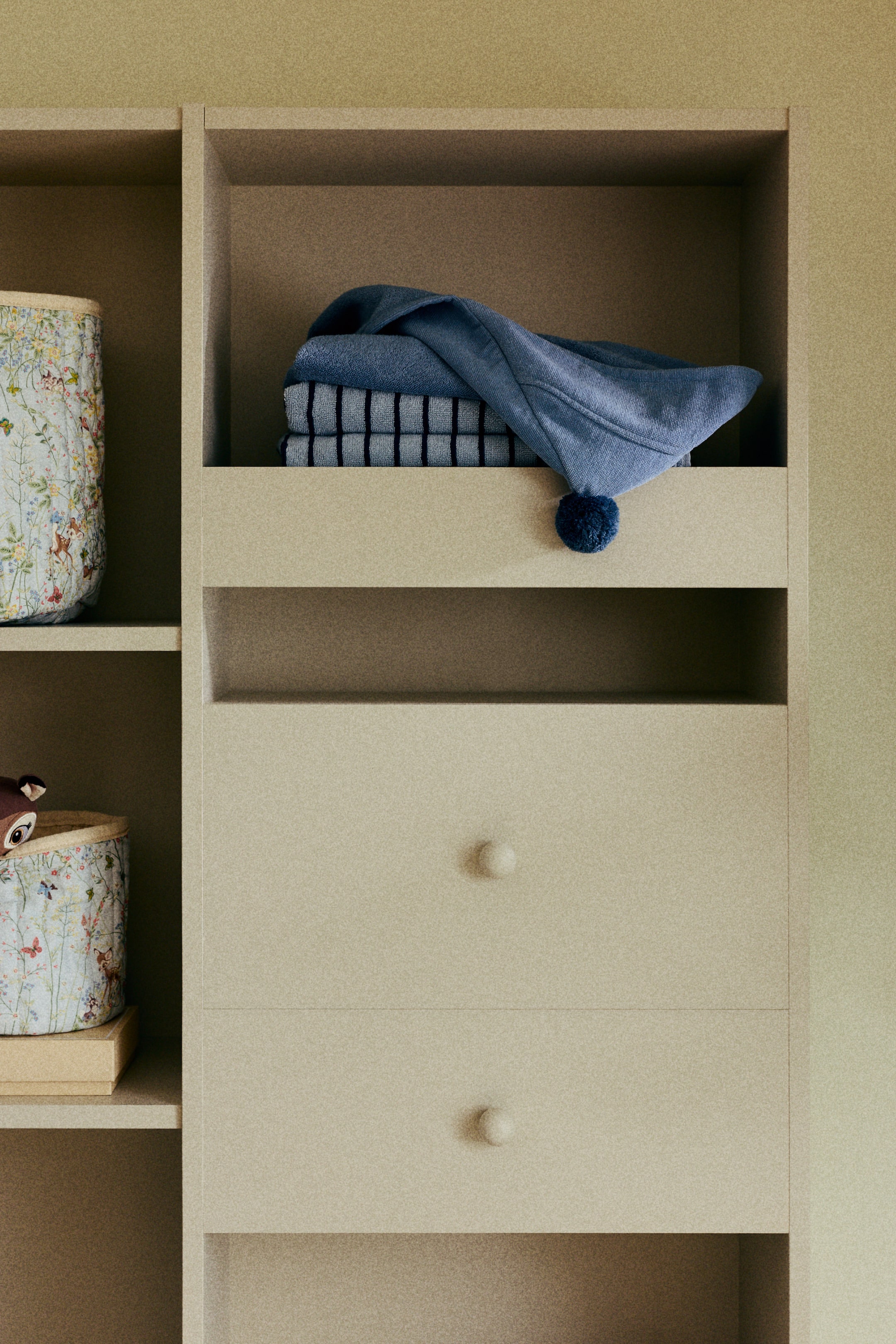 View larger image: A blue hooded bath towel is folded, featuring a dark blue pom-pom on the corner of its hood.